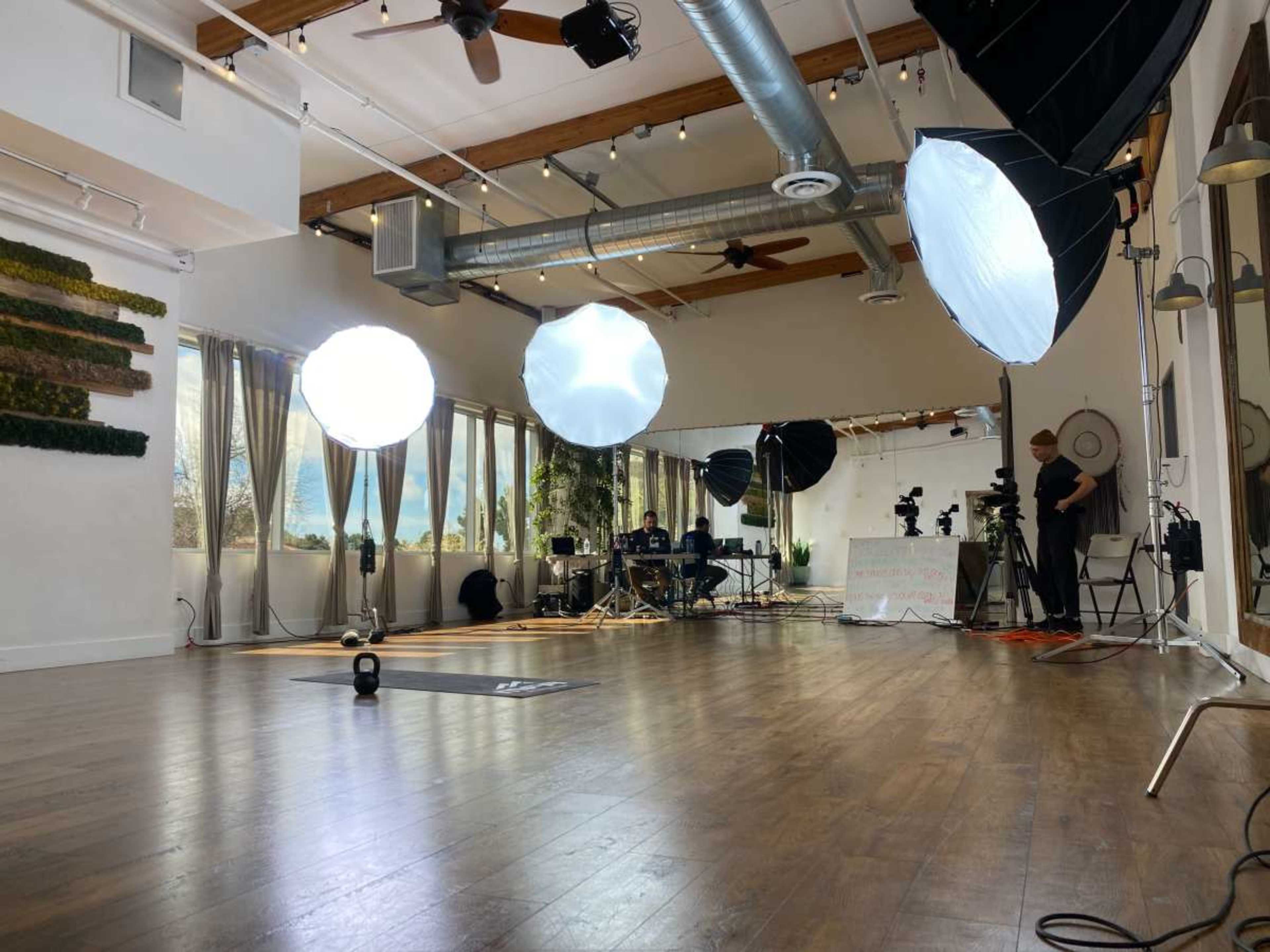 A spacious interior studio is set up with large softbox lights, a mirrored wall, and various filming equipment arranged for a production.