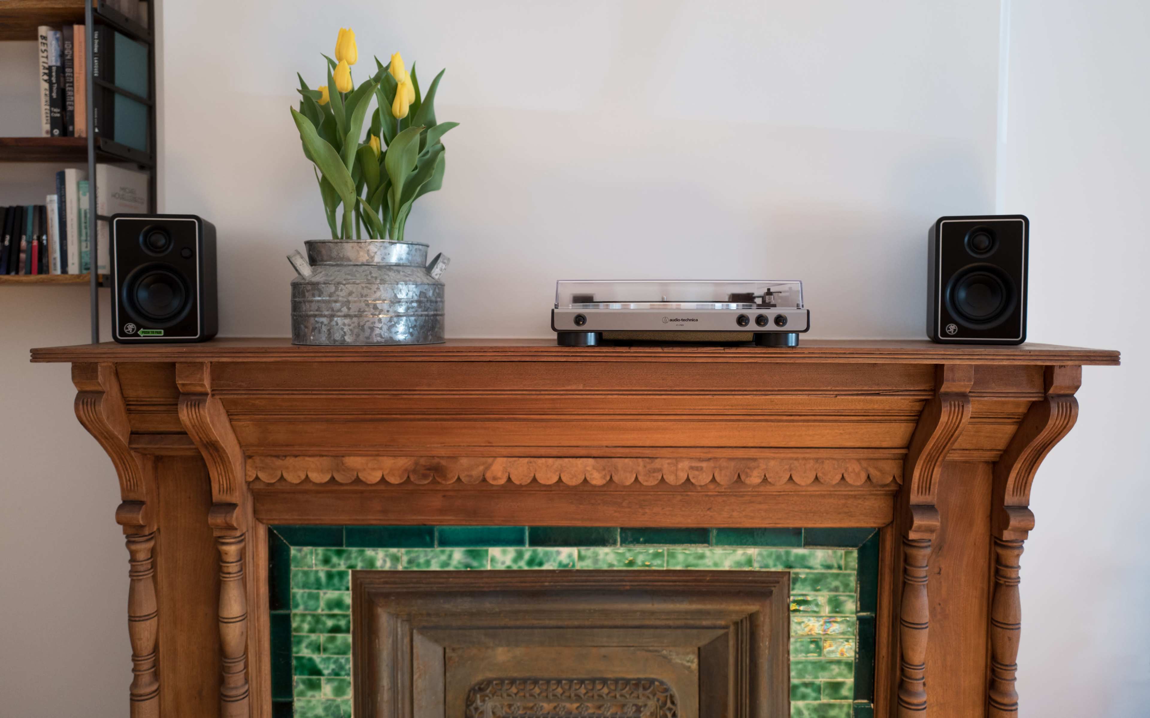 A wooden mantel displays a turntable and speakers on either side, with a metal planter of yellow tulips in the center.