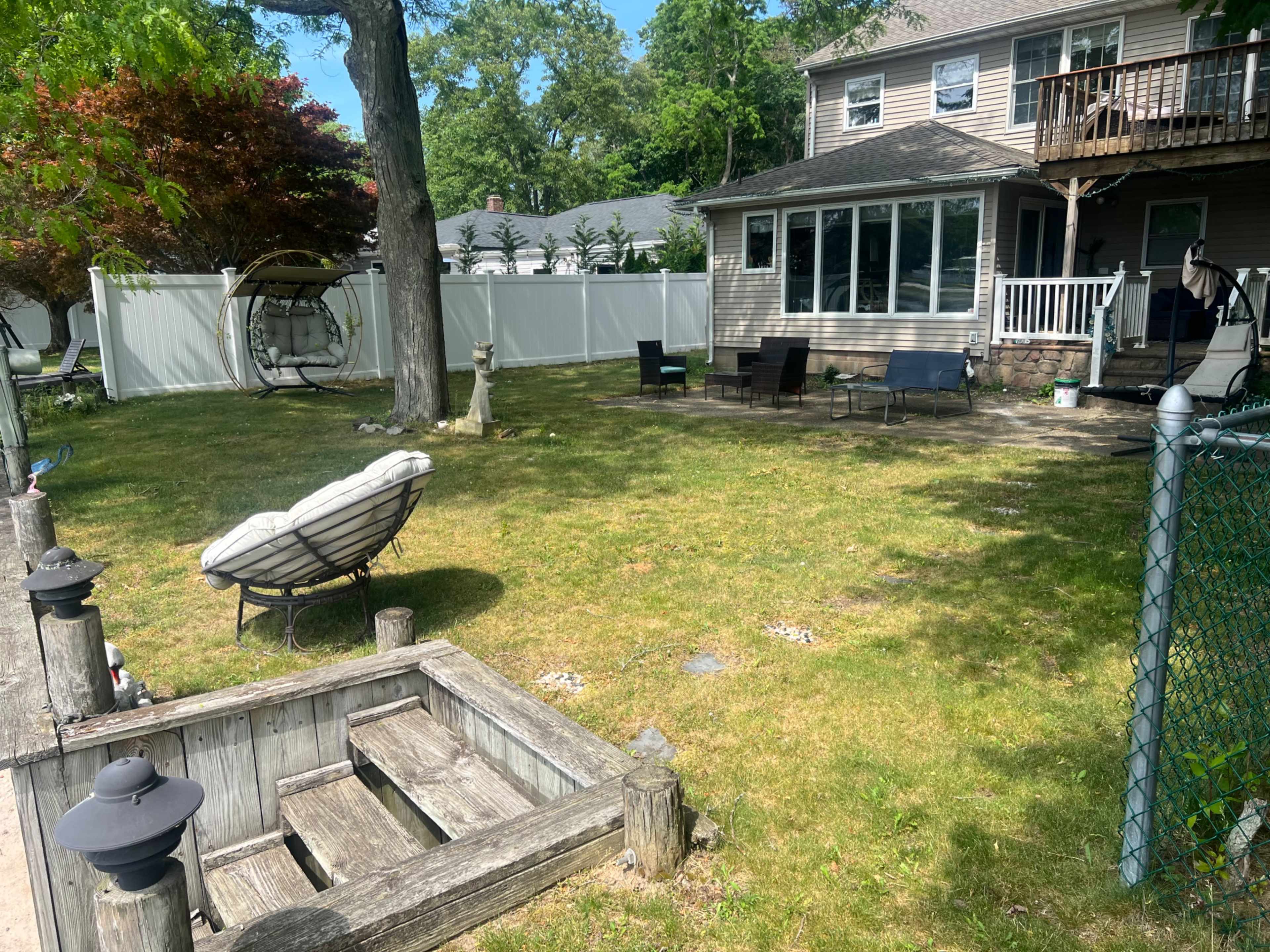 The image shows a backyard with a lawn, a swing chair, lounge chairs, a fence, and a two-story house in the background.