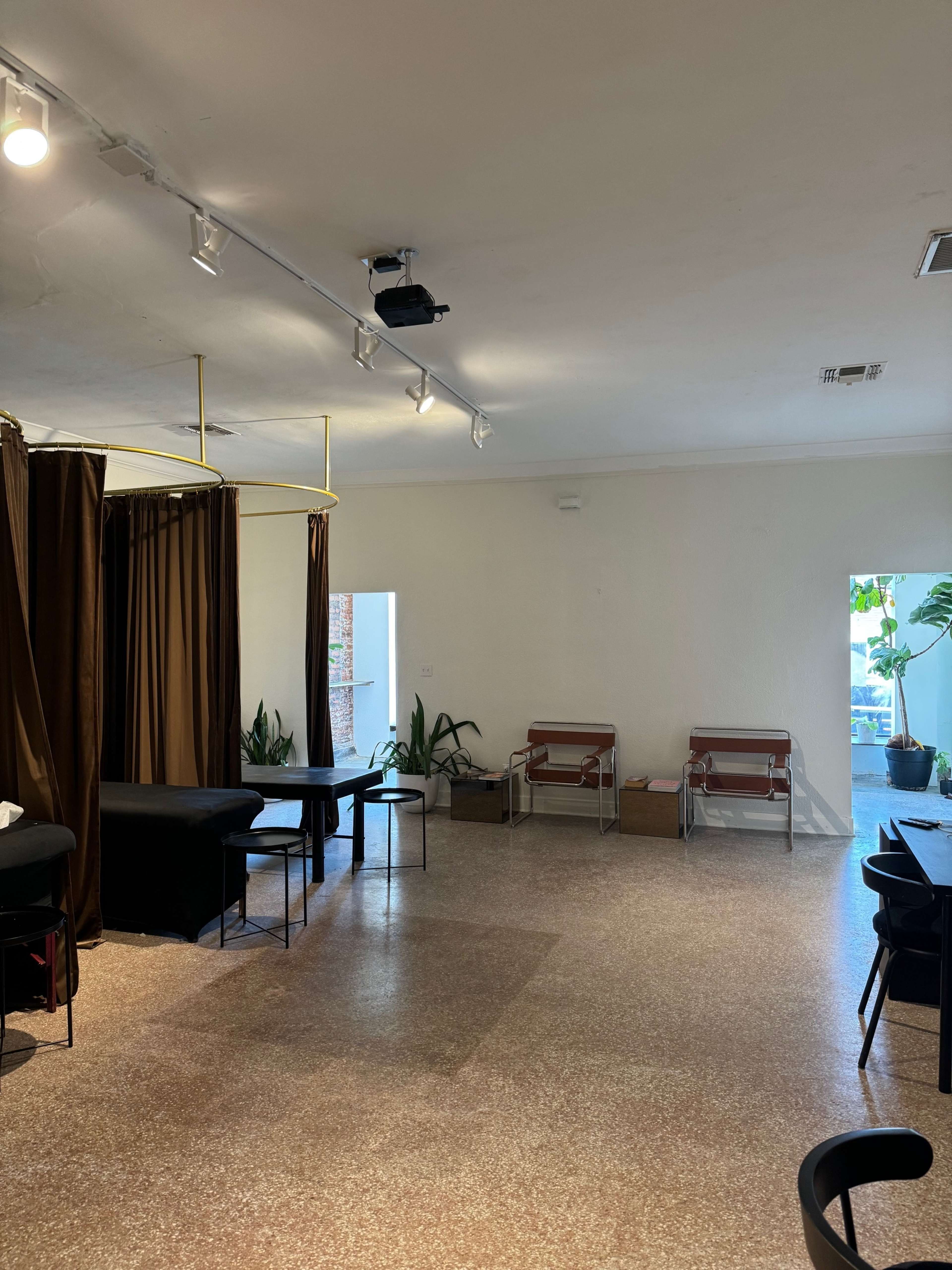 A spacious, well-lit interior with seating areas and plants, featuring a combination of black furniture and brown curtains.