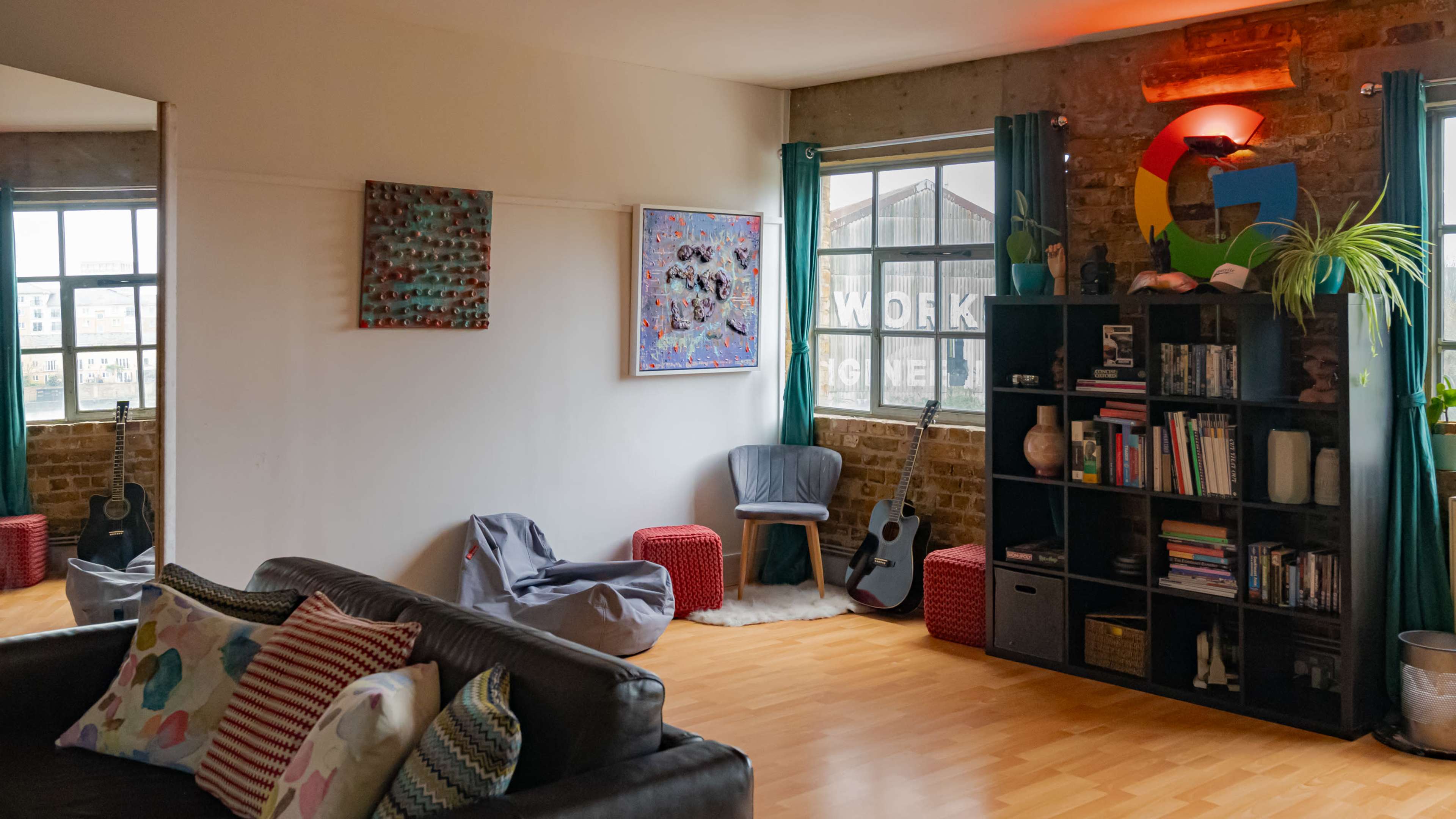 A cozy living room with a sofa, a bookshelf, a guitar, and various artworks on the walls.