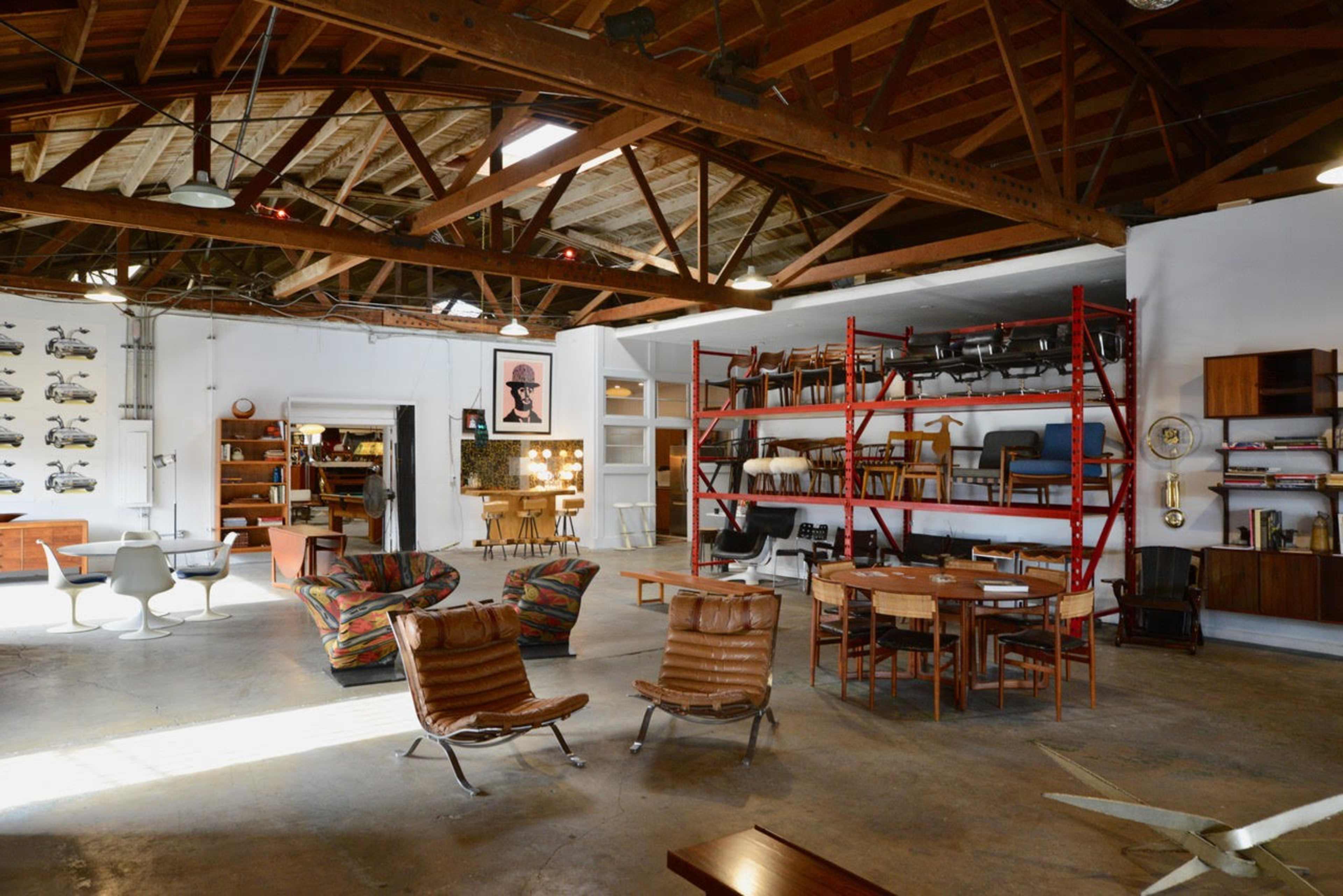 An open, stylish interior space with various furniture pieces, including colorful armchairs, wooden tables, and shelves filled with books and decor.