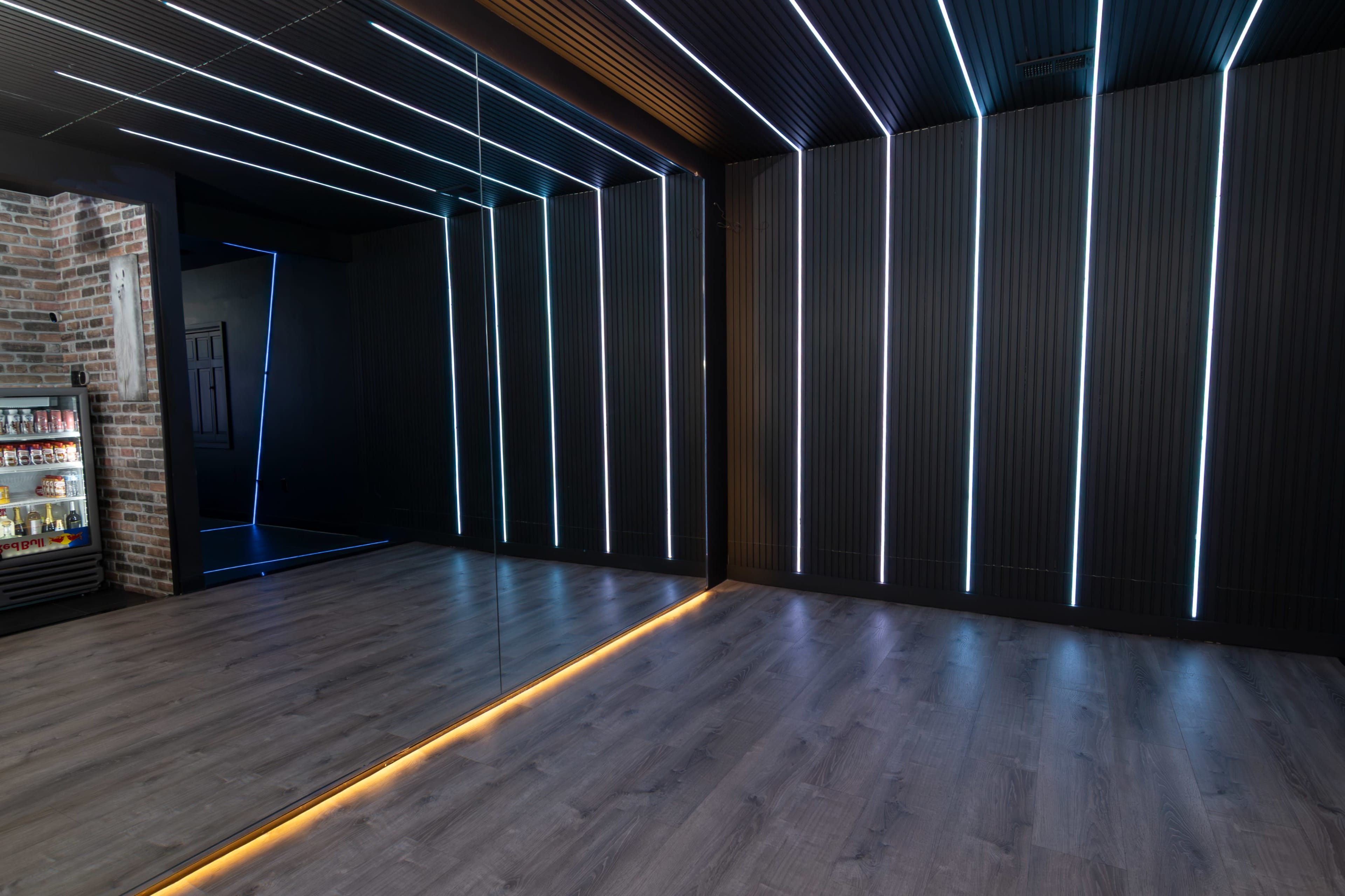 The image shows a modern interior space featuring dark walls with vertical LED light strips and a mirrored wall, alongside a wooden floor.