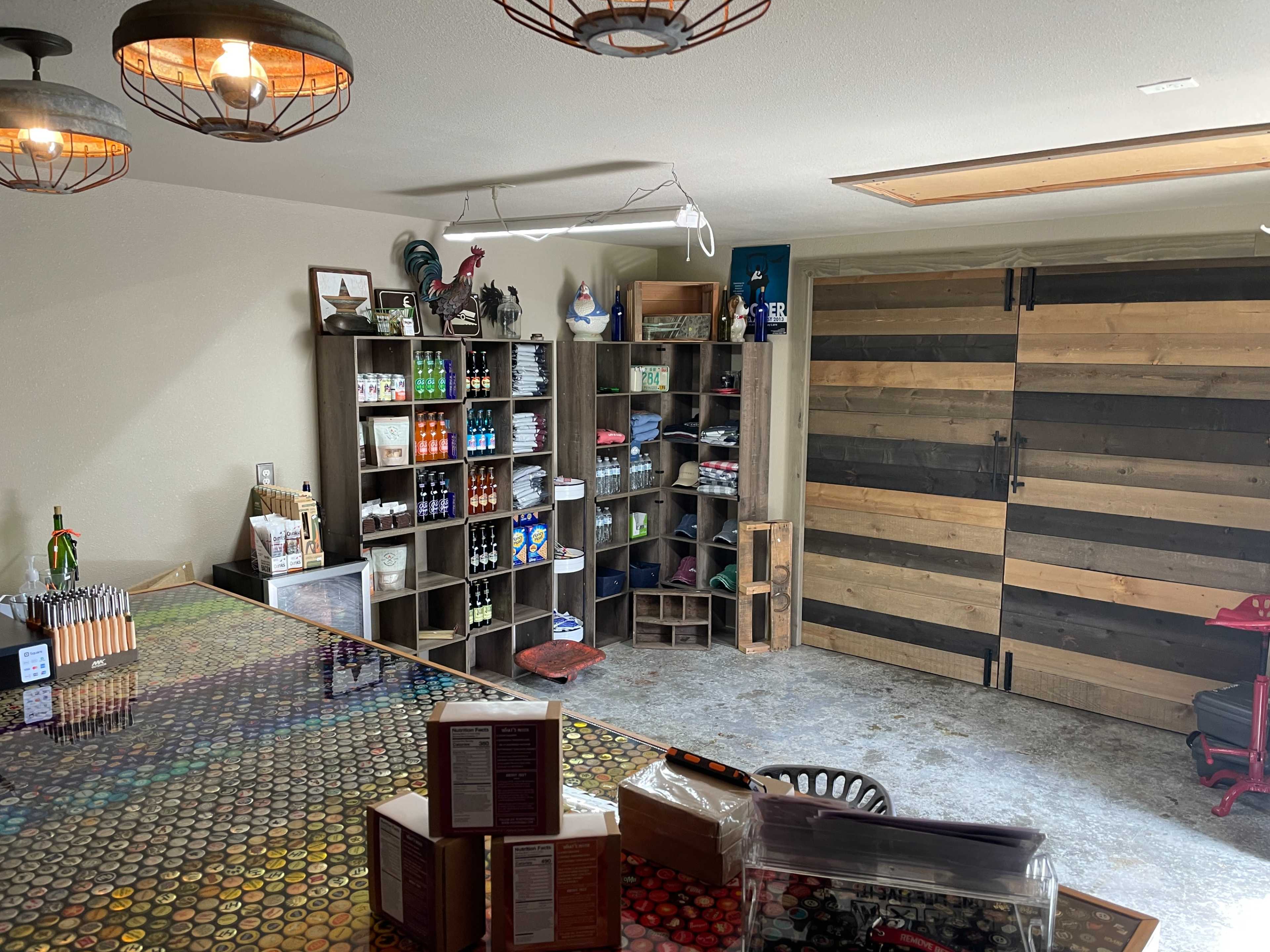 A workshop space featuring shelving units stocked with various paint supplies, a table with organized materials, and large wooden doors in the background.