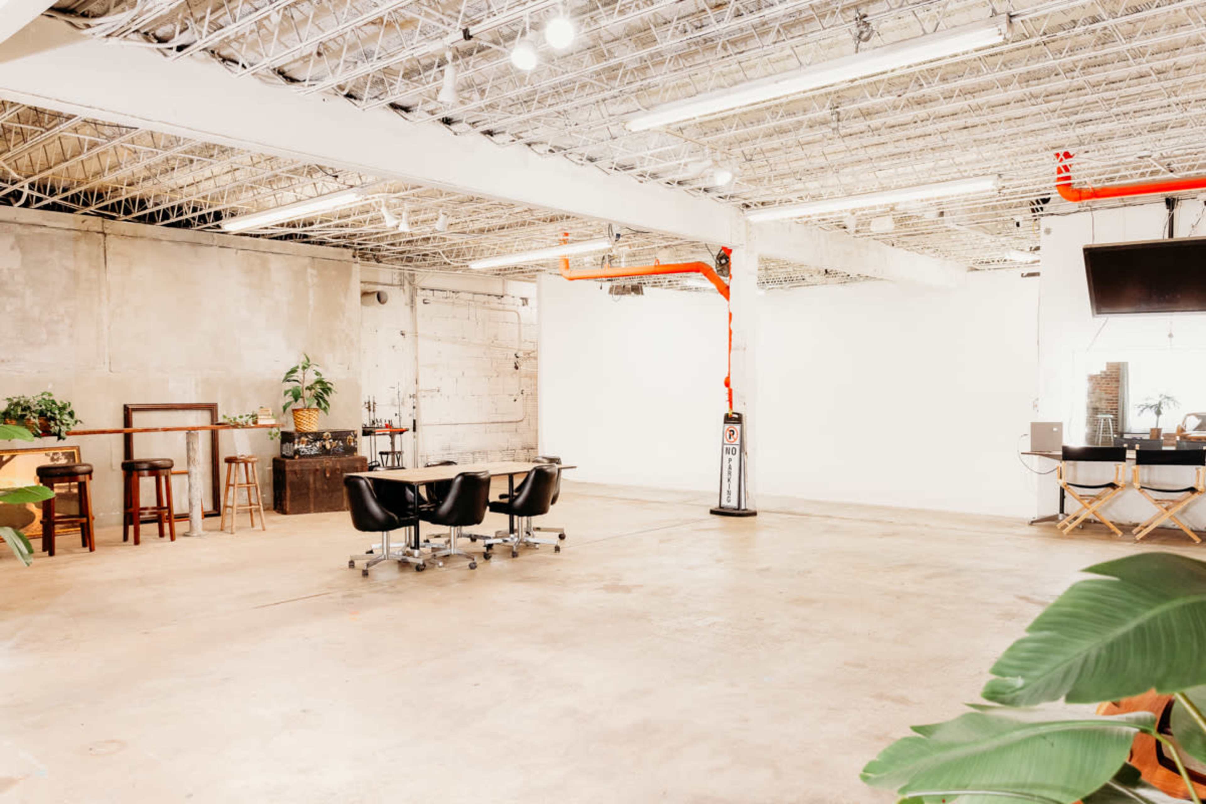 An empty, modern office space featuring various seating arrangements, plants, and exposed ceiling infrastructure.