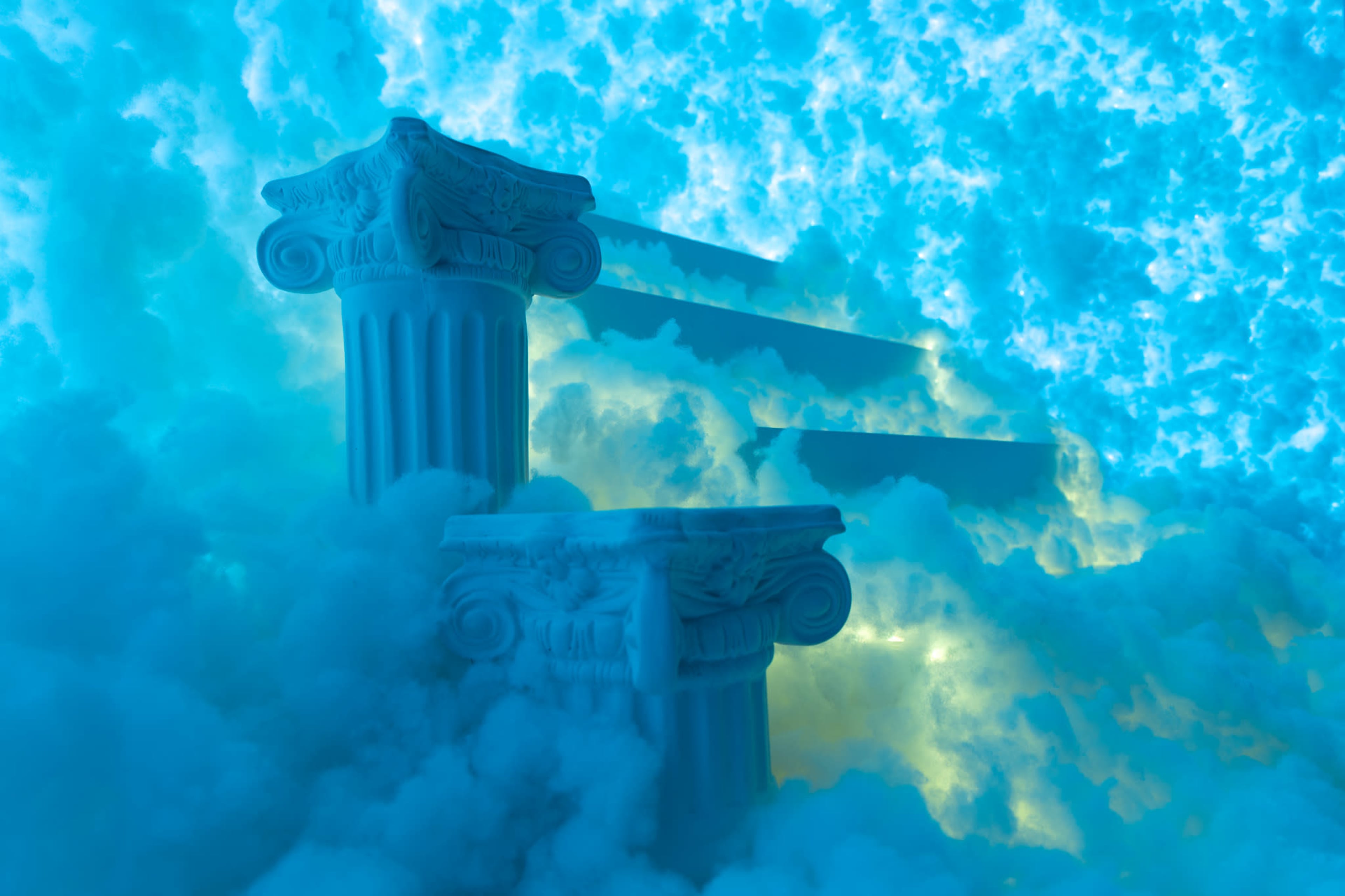 Two classical columns partially submerged in blue and white mist, with illuminated steps visible in the background.