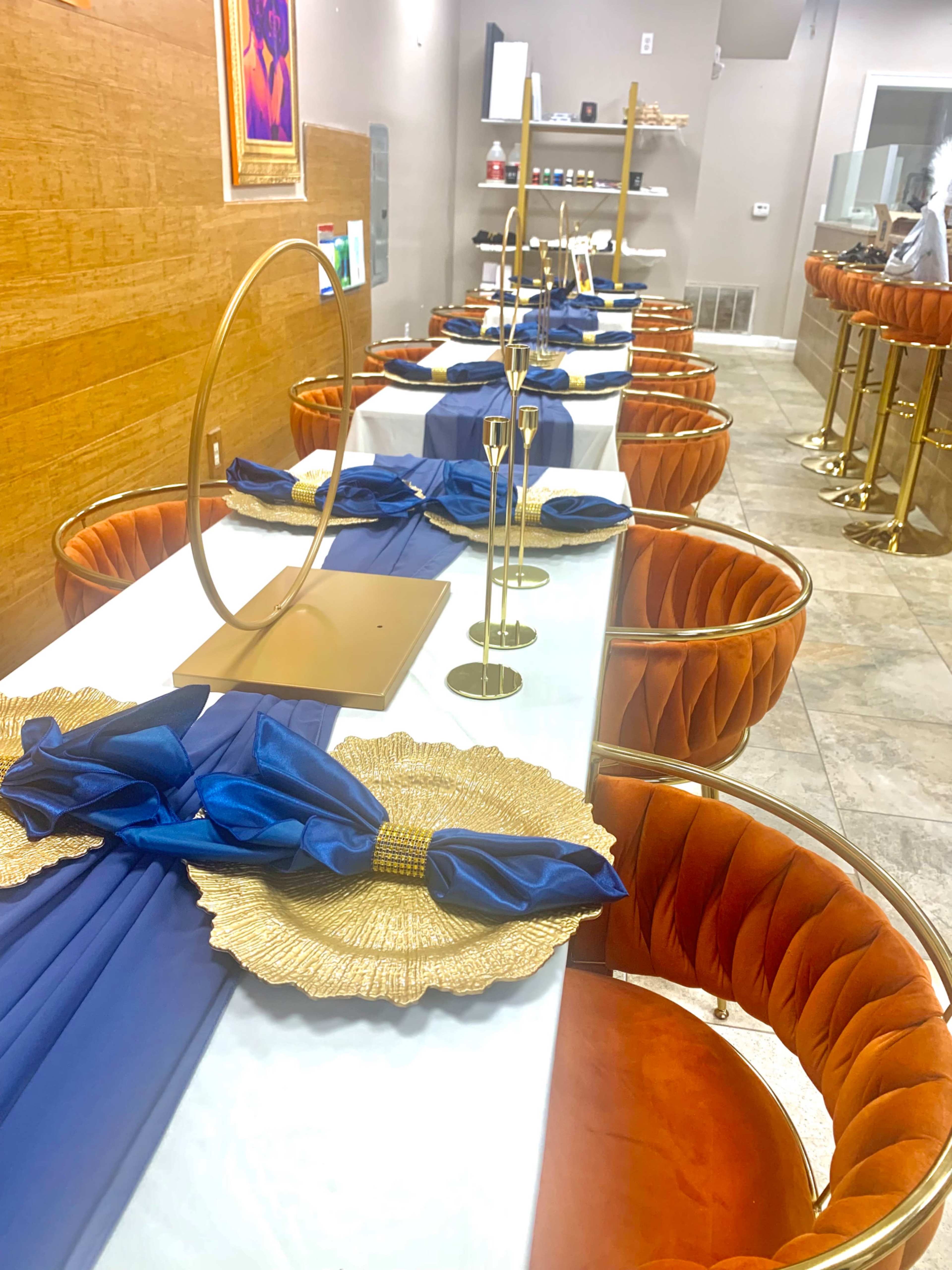 A dining area with neatly arranged tables featuring blue table runners, gold decor, and orange upholstered chairs.