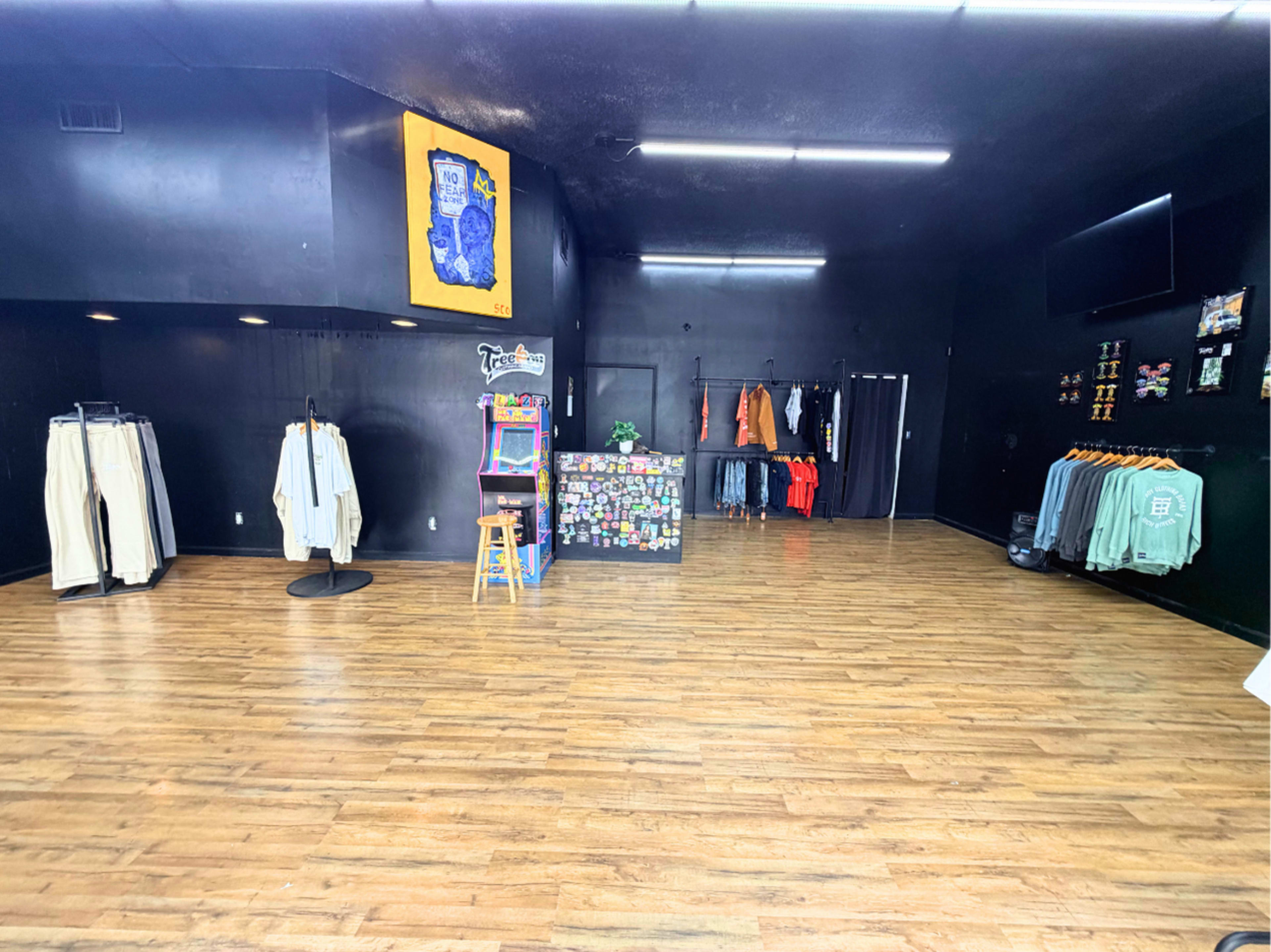 The image shows an empty retail space with wooden flooring, featuring clothing displayed on racks and a colorful checkout counter at the center.