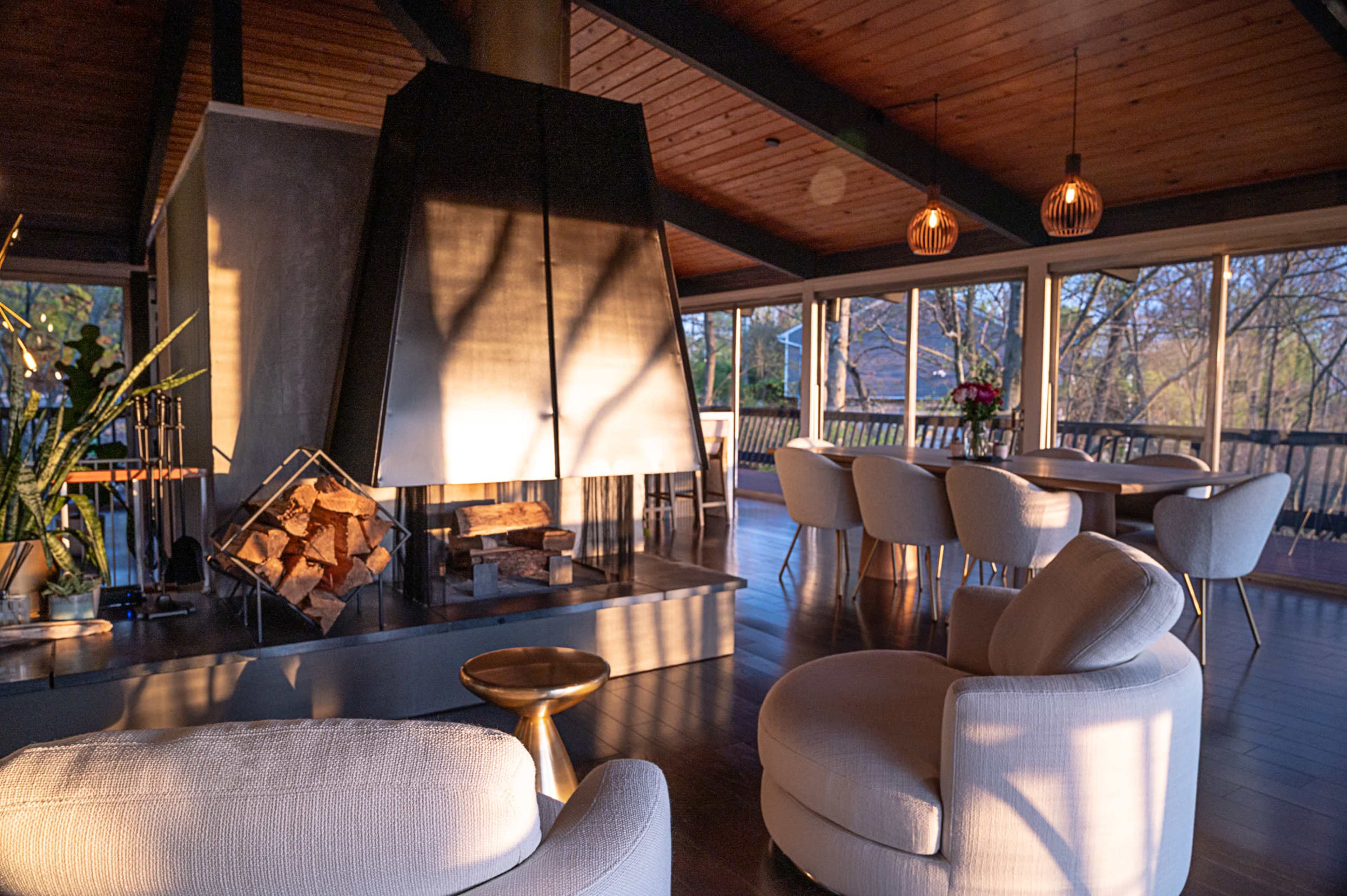 A modern living space featuring a large black fireplace, comfortable seating, and a dining area with a table set for several people, illuminated by natural light.