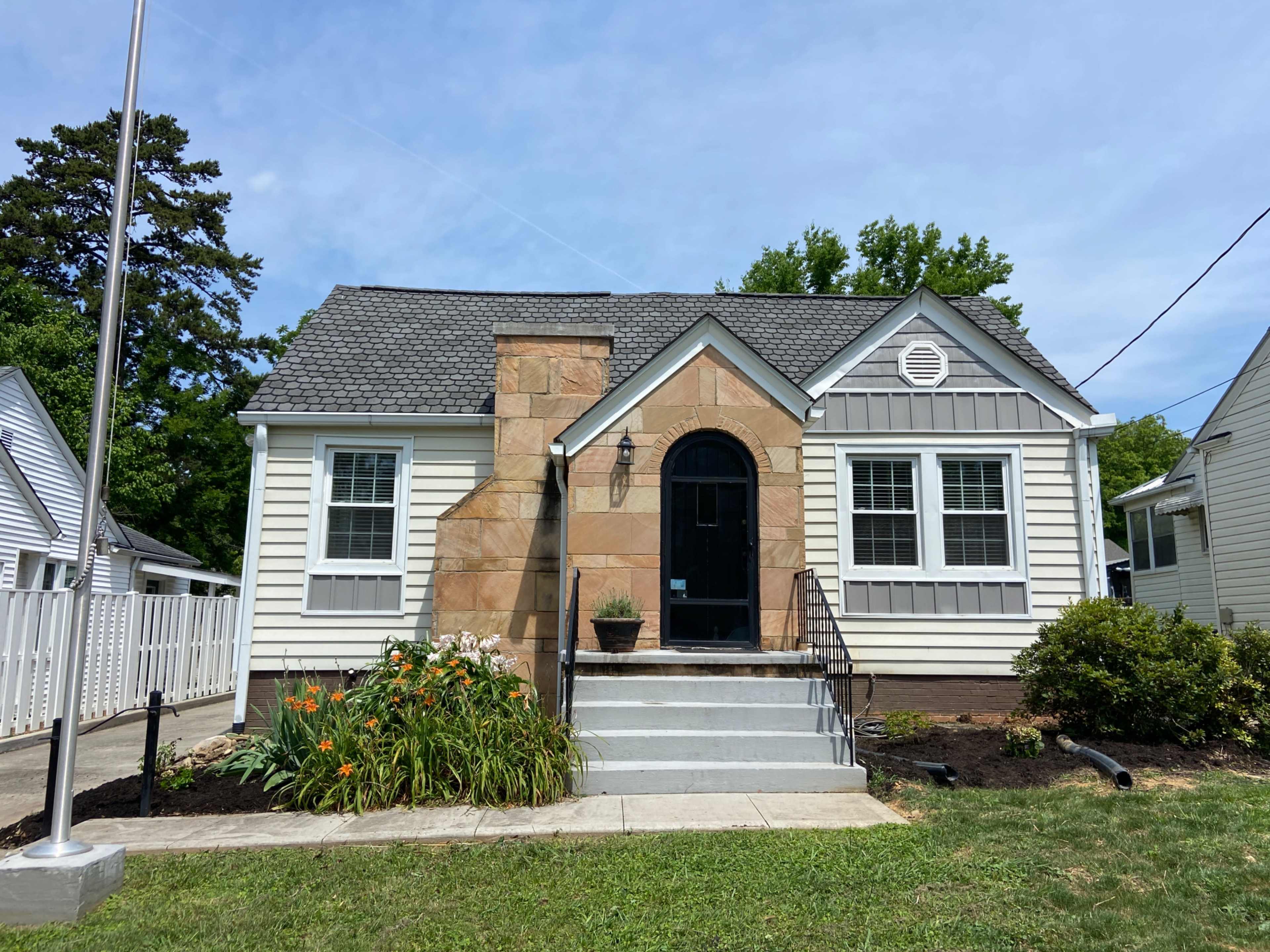 A single-story house with a stone accent wall, gray shingles, and a small front garden.