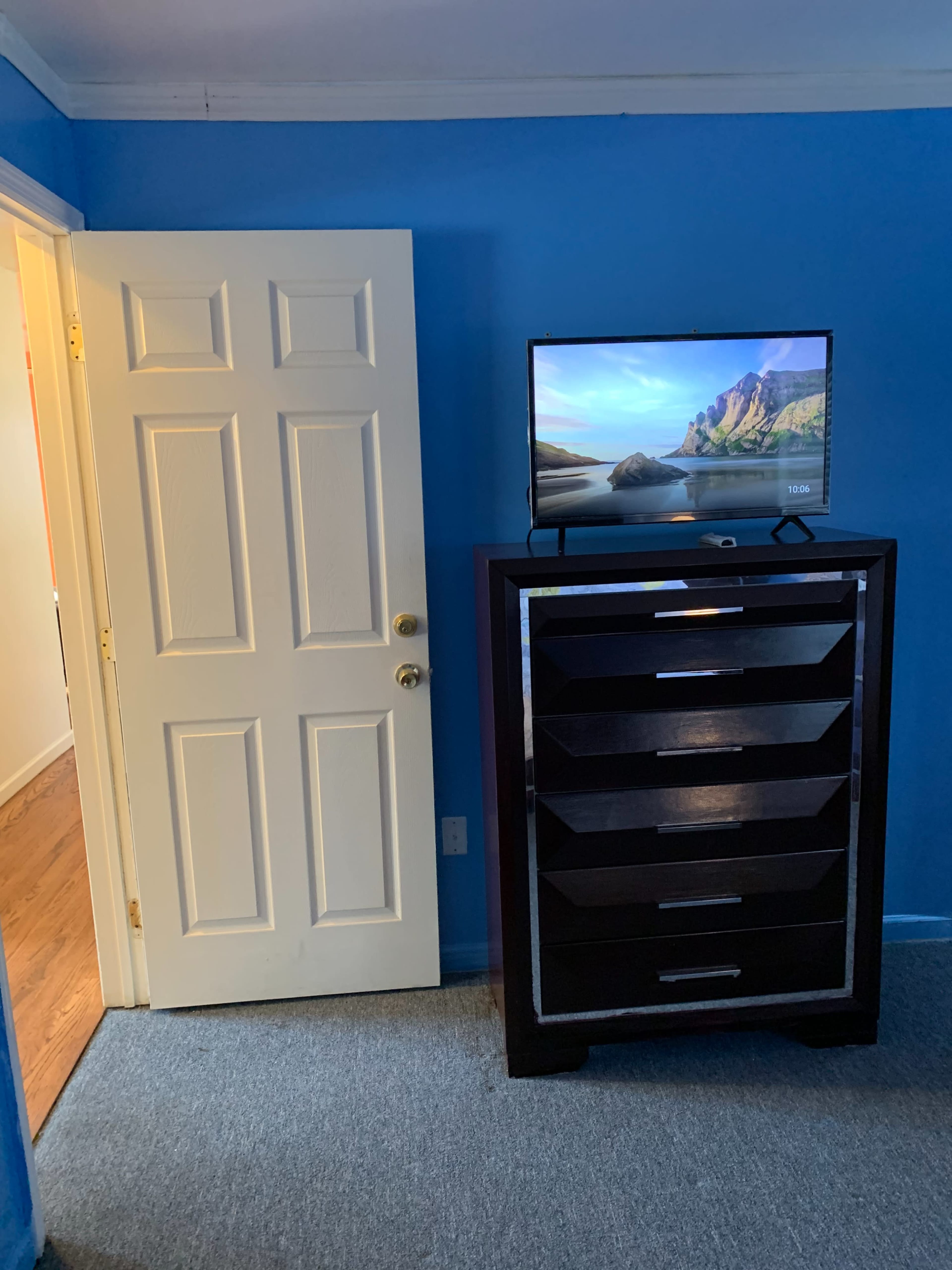 A blue-walled room features a closed door on the left and a tall dresser with a television on top in front of it.