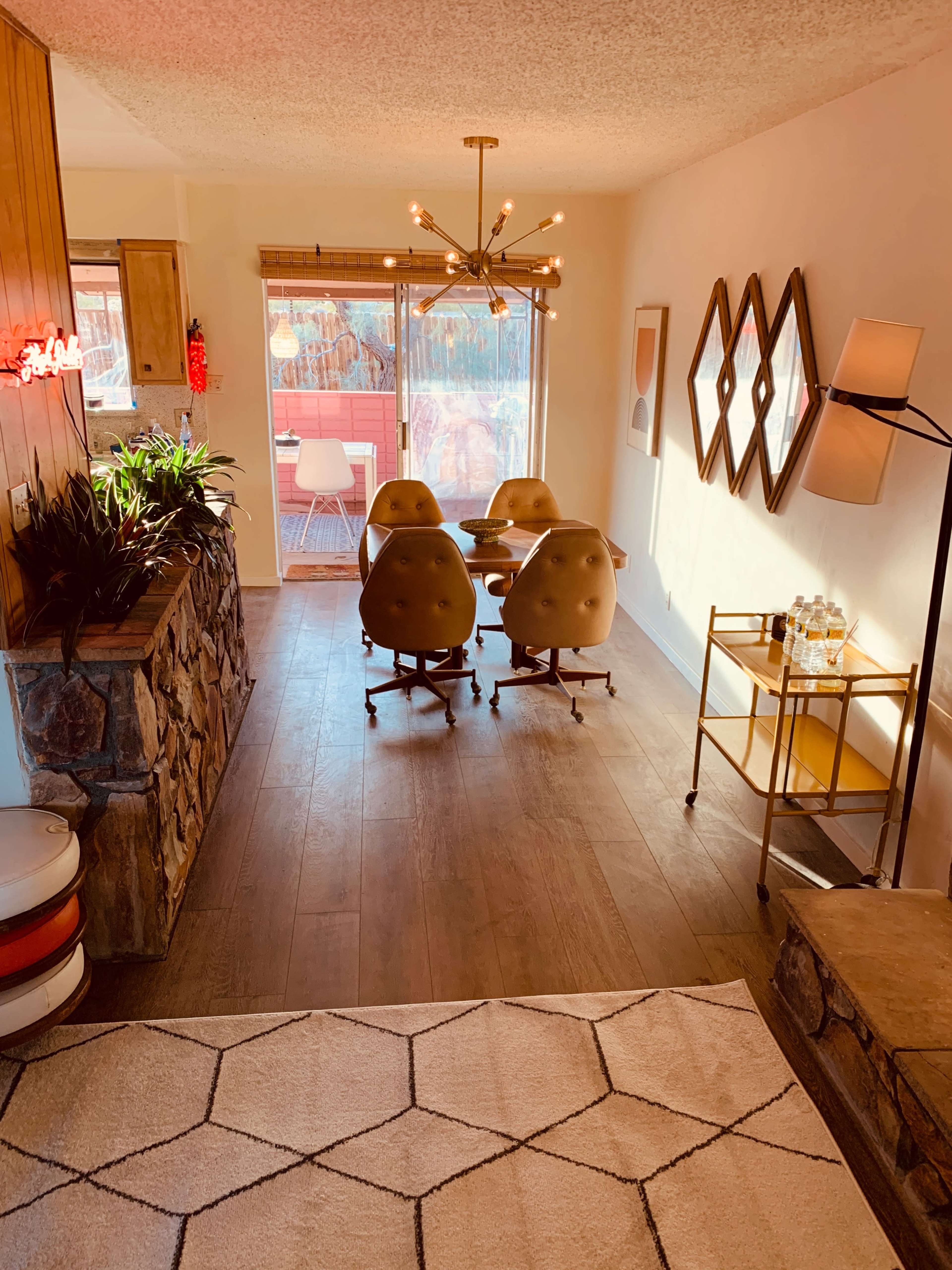 A modern dining area features a glass table with round, brown chairs, surrounded by wood-paneled walls and large windows overlooking a patio.