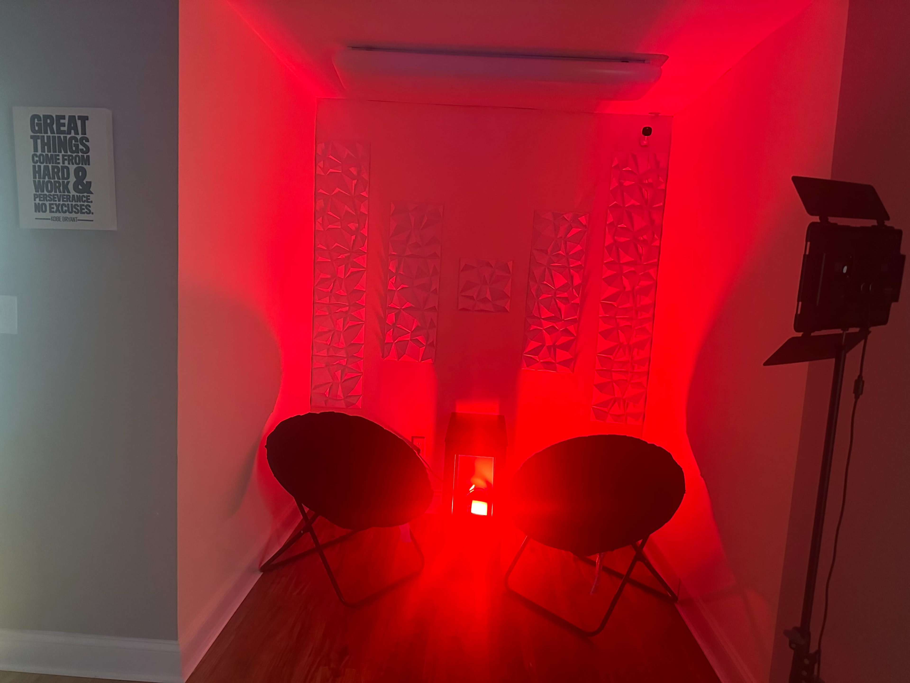 The image features a room illuminated in red light with two black chairs facing a central illuminated object and decorated with textured white walls.