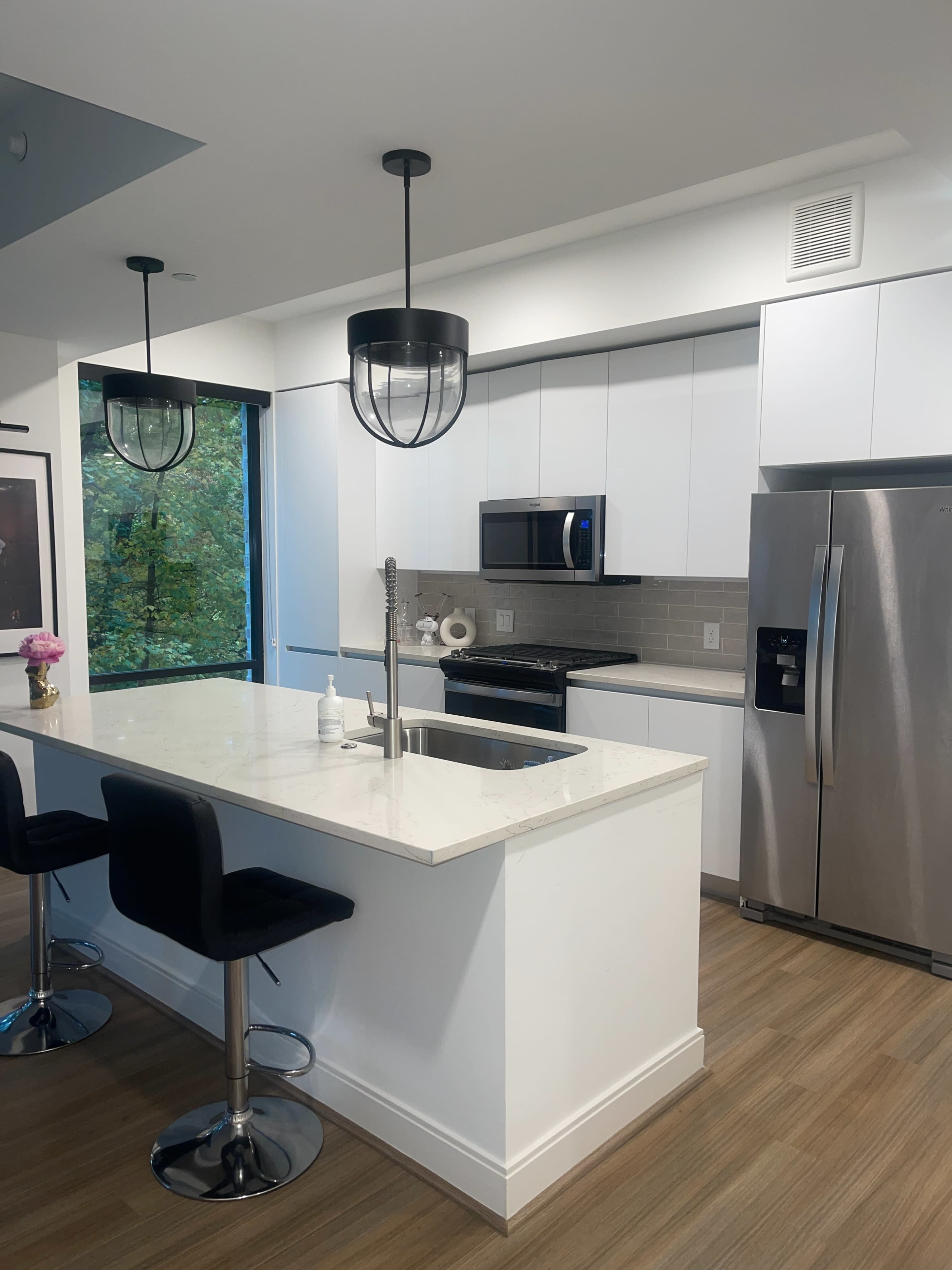 A modern kitchen features white cabinets, stainless steel appliances, and a central island with bar stools.