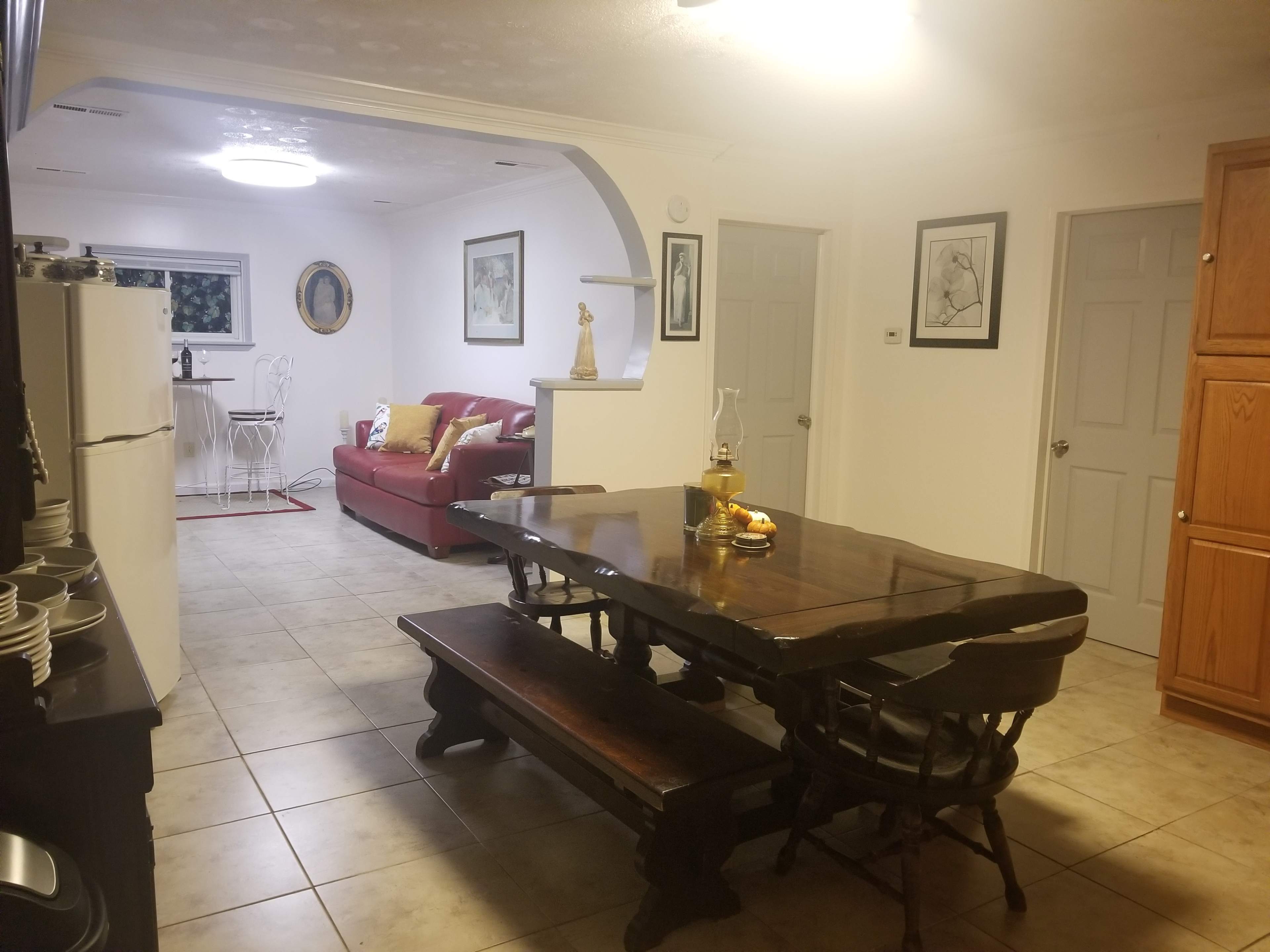 A living space with a dining table, a red sofa, and a kitchen area featuring a refrigerator and cabinets.