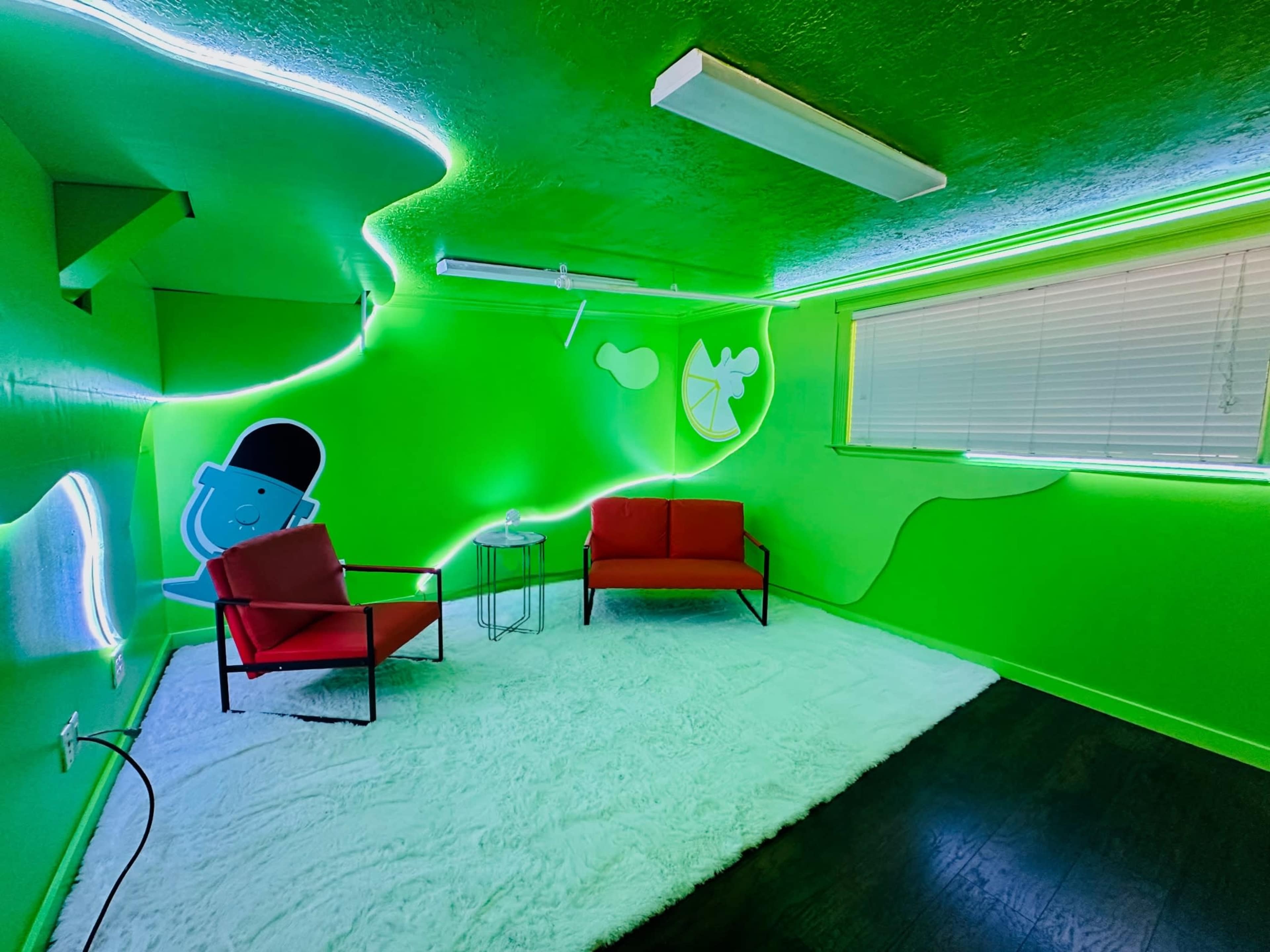 The image shows a brightly lit green room with two red chairs, a small table, and decorative wall elements.