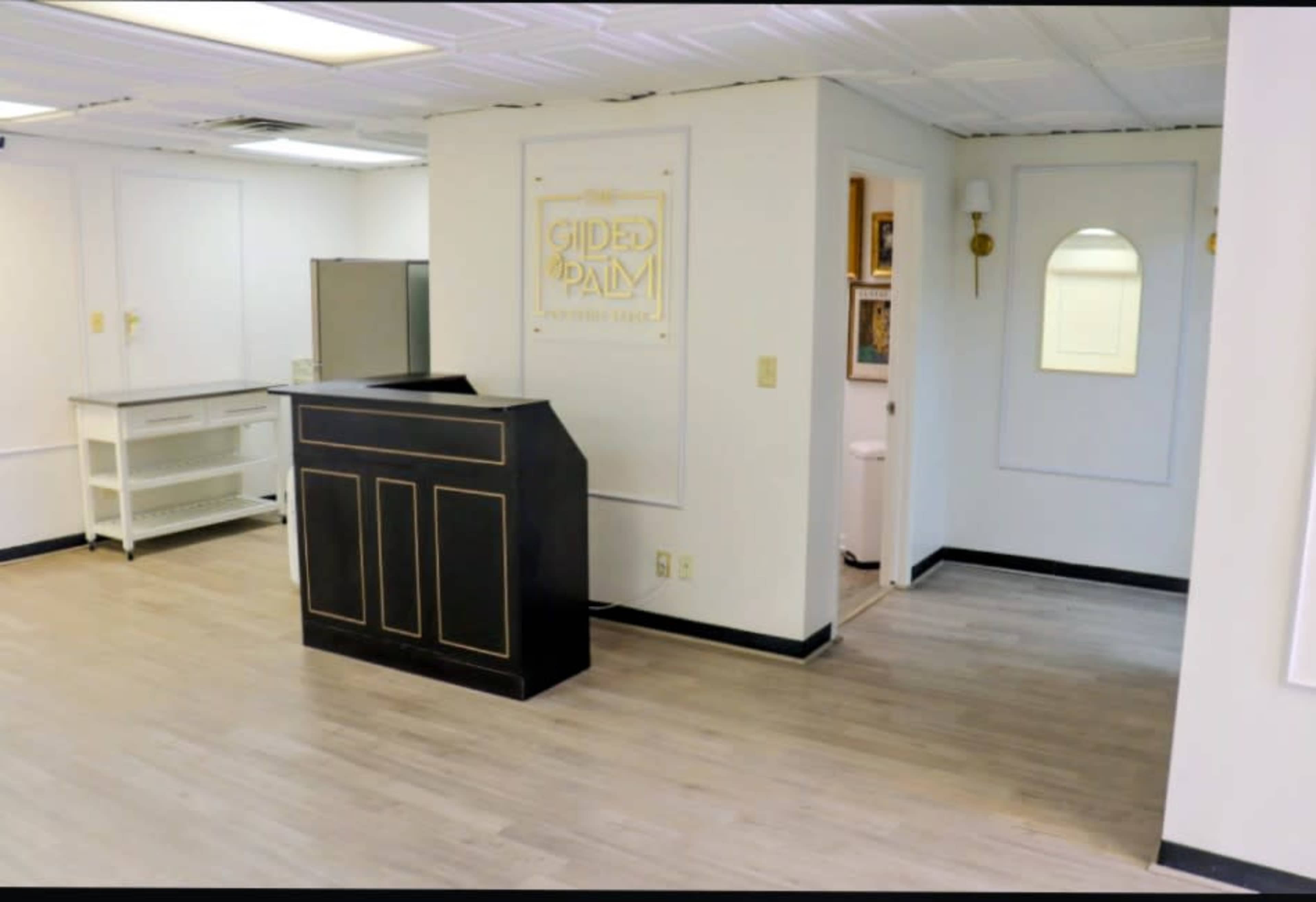 The image shows a reception area with a black front desk, white walls, and a small adjoining room visible through an arched mirror.