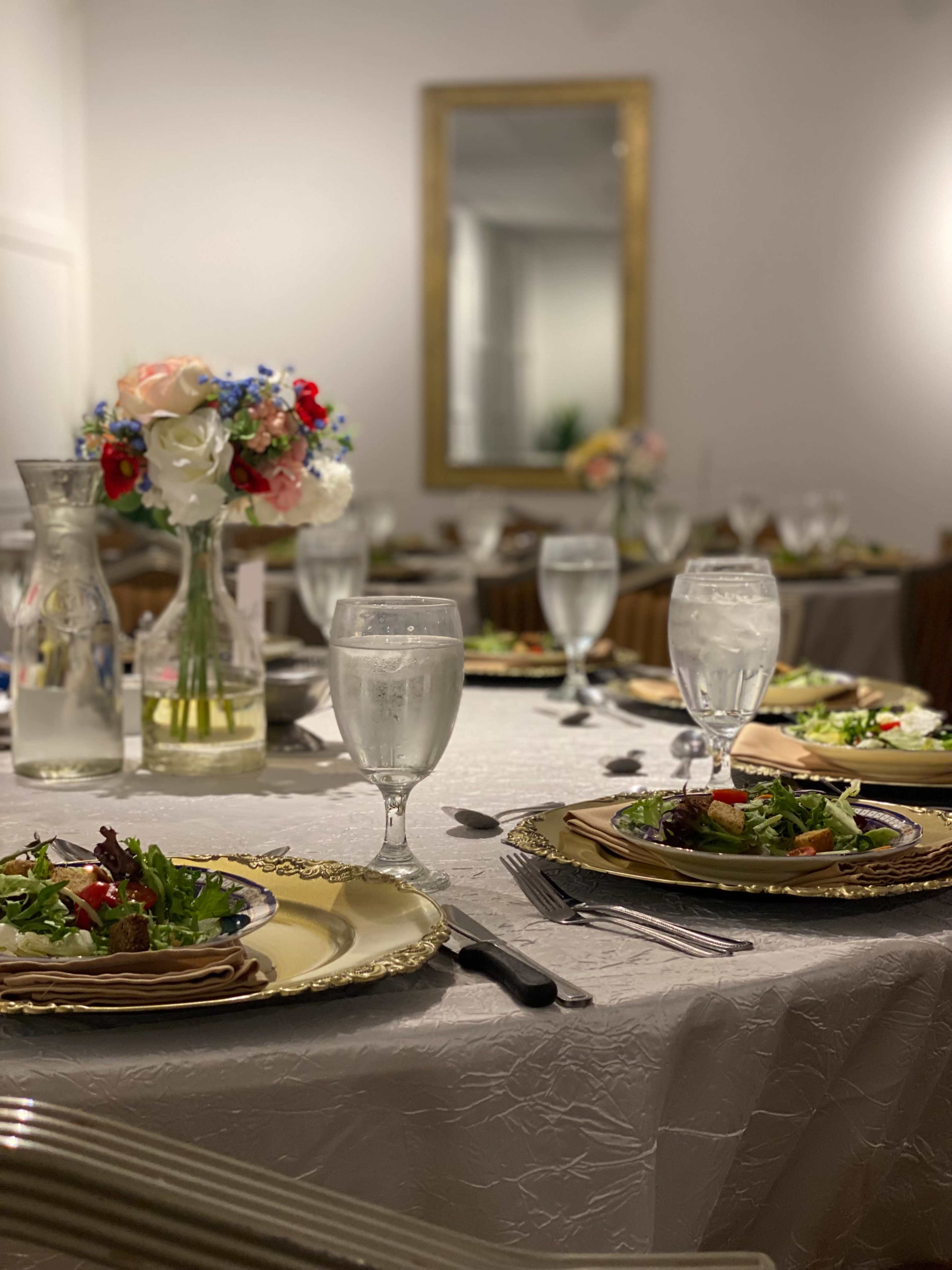 A formal dining setup features elegantly arranged plates, glasses of water, and floral centerpieces on a tablecloth.