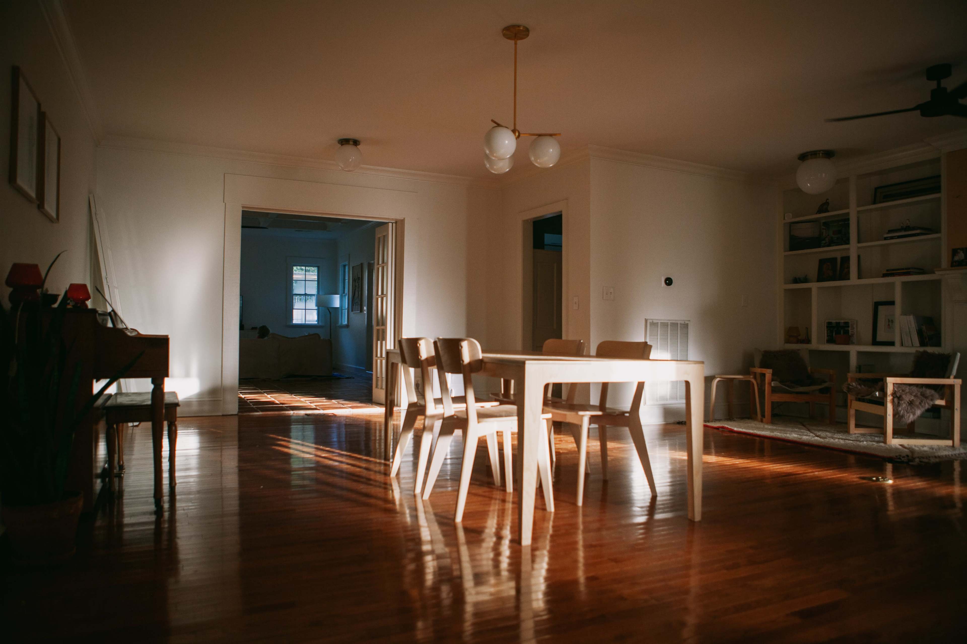 A dining area features a wooden table surrounded by chairs, illuminated by natural light streaming in from a nearby window.