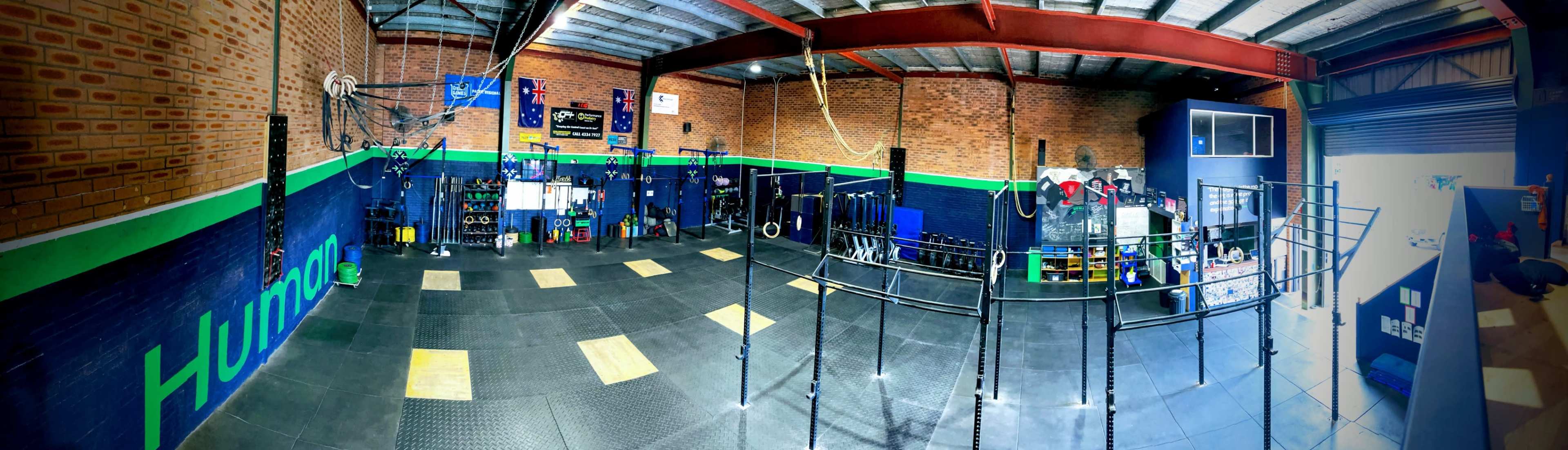 An indoor gym space with various exercise equipment, including pull-up bars and weightlifting stations, arranged in a spacious area with a rubber floor and brick walls.