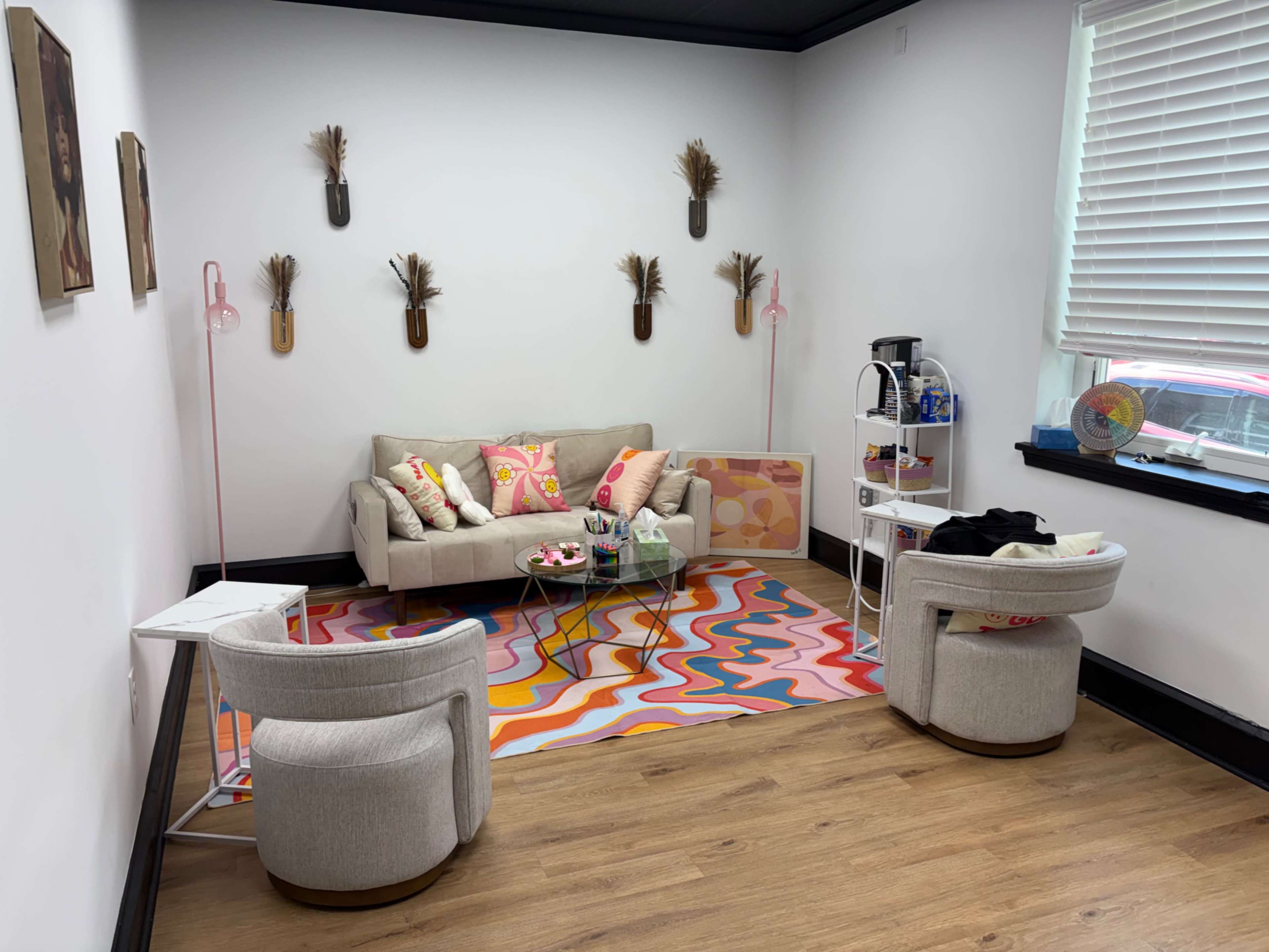 The image shows a cozy, modern sitting area with a beige sofa, colorful rug, two armchairs, and decorative wall art.