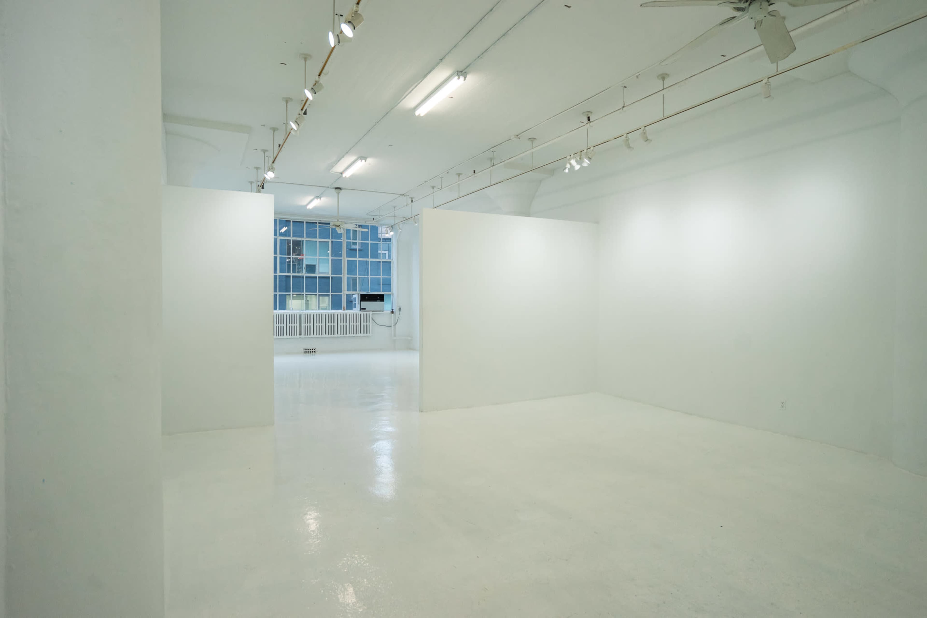 A spacious, minimalist art gallery with white walls and a glossy floor, illuminated by overhead lighting.