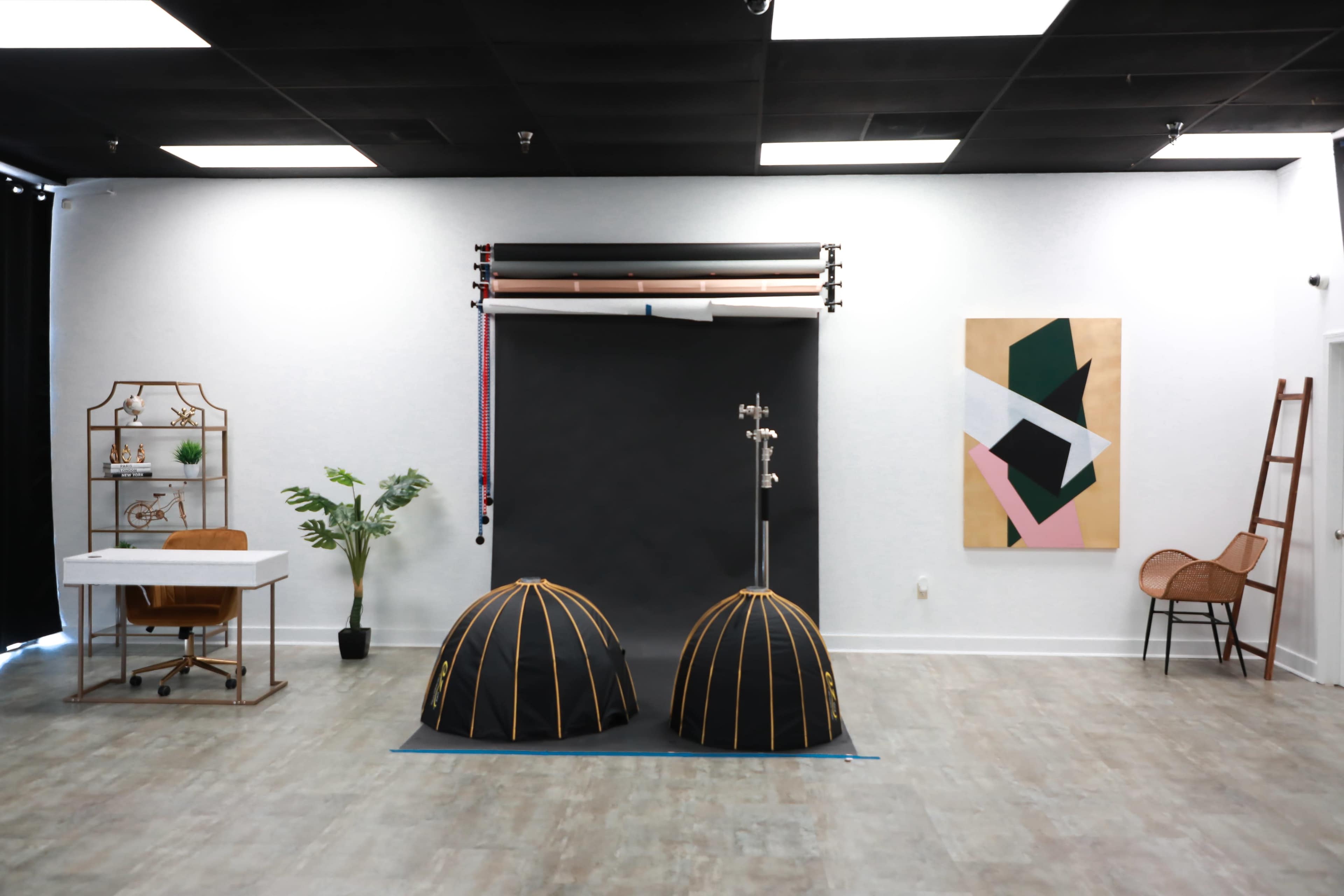 The image features a spacious studio with two dome-shaped light tents, a backdrop stand, a desk with a chair, plants, and wall art.