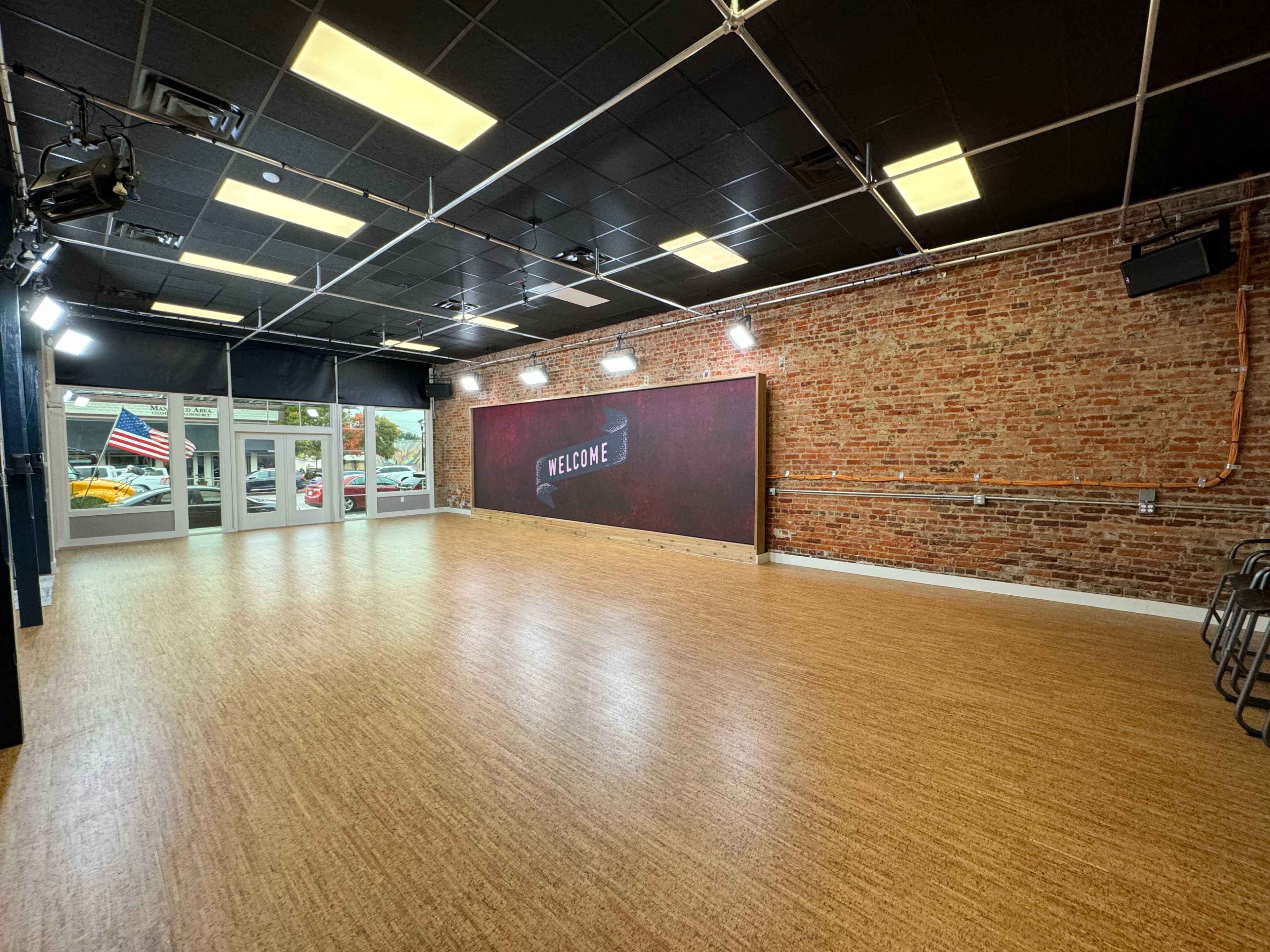A spacious, empty room with a brick wall and a large "WELCOME" sign, illuminated by overhead lights.