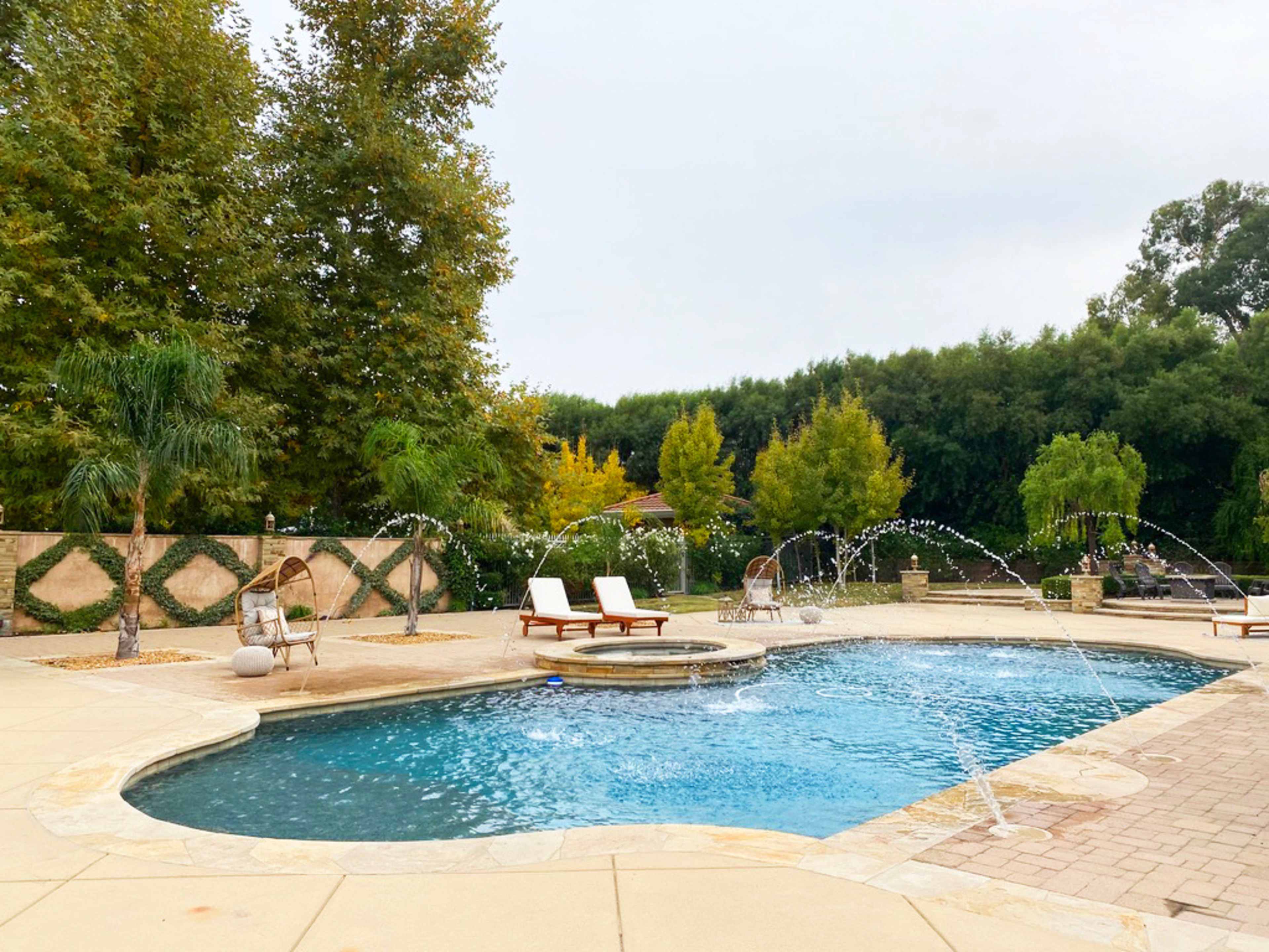 A swimming pool with a spa area features water fountains, surrounded by lounge chairs and landscaped greenery.