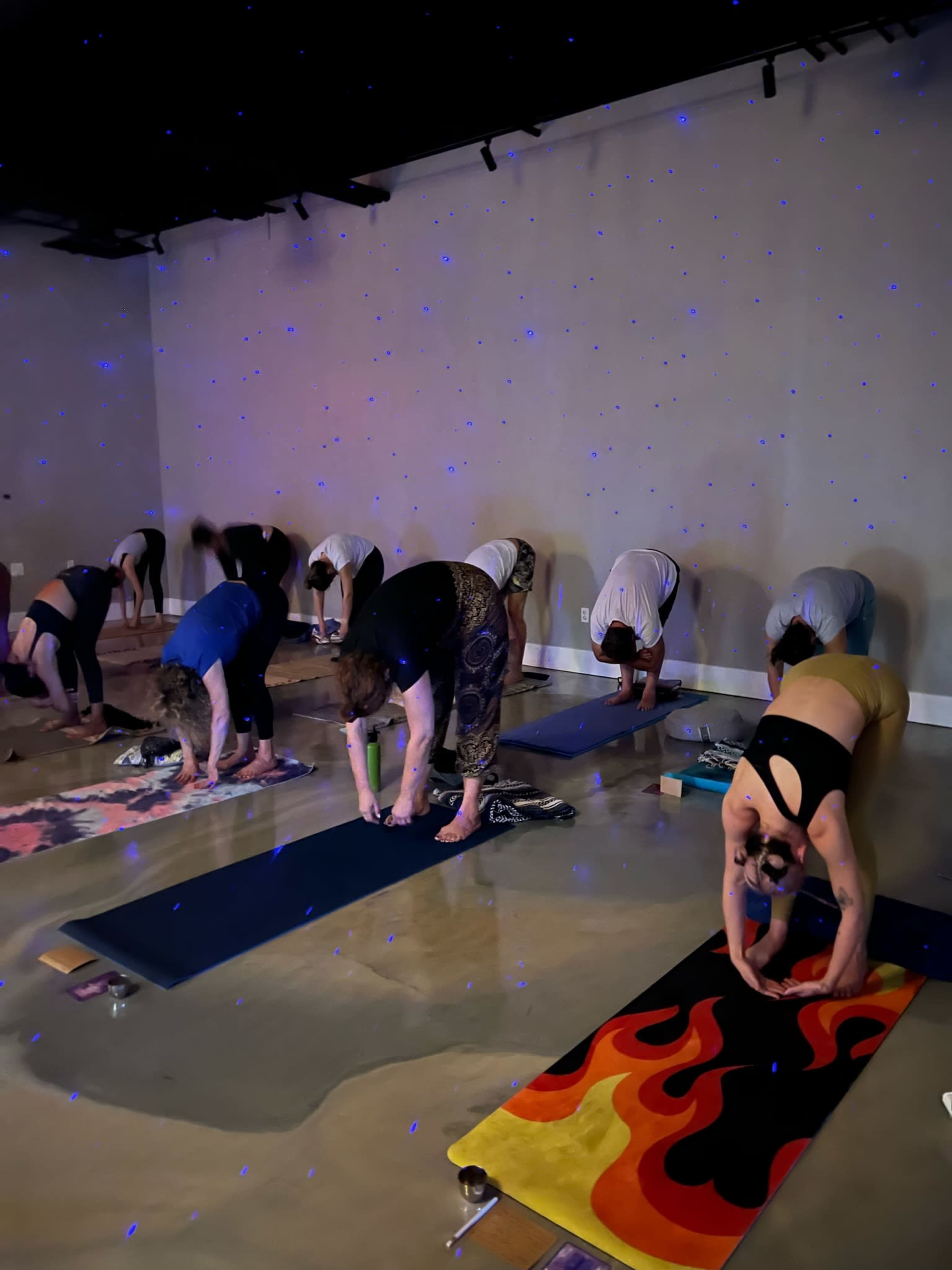 A group of people is practicing yoga in a dimly lit studio with blue stars projected on the walls.