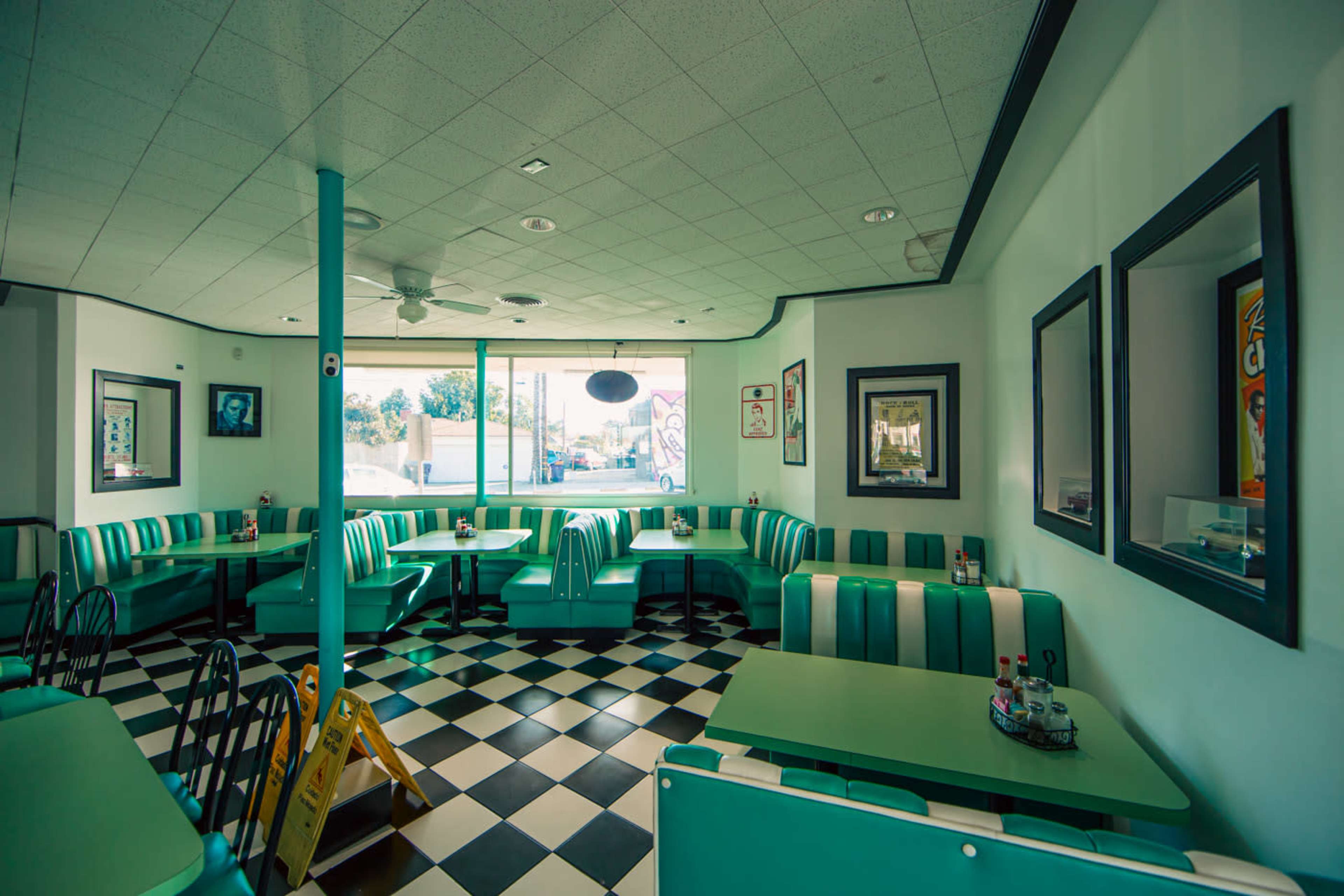 The image shows a retro-style diner interior with teal and white booth seating, checkered flooring, and large windows.