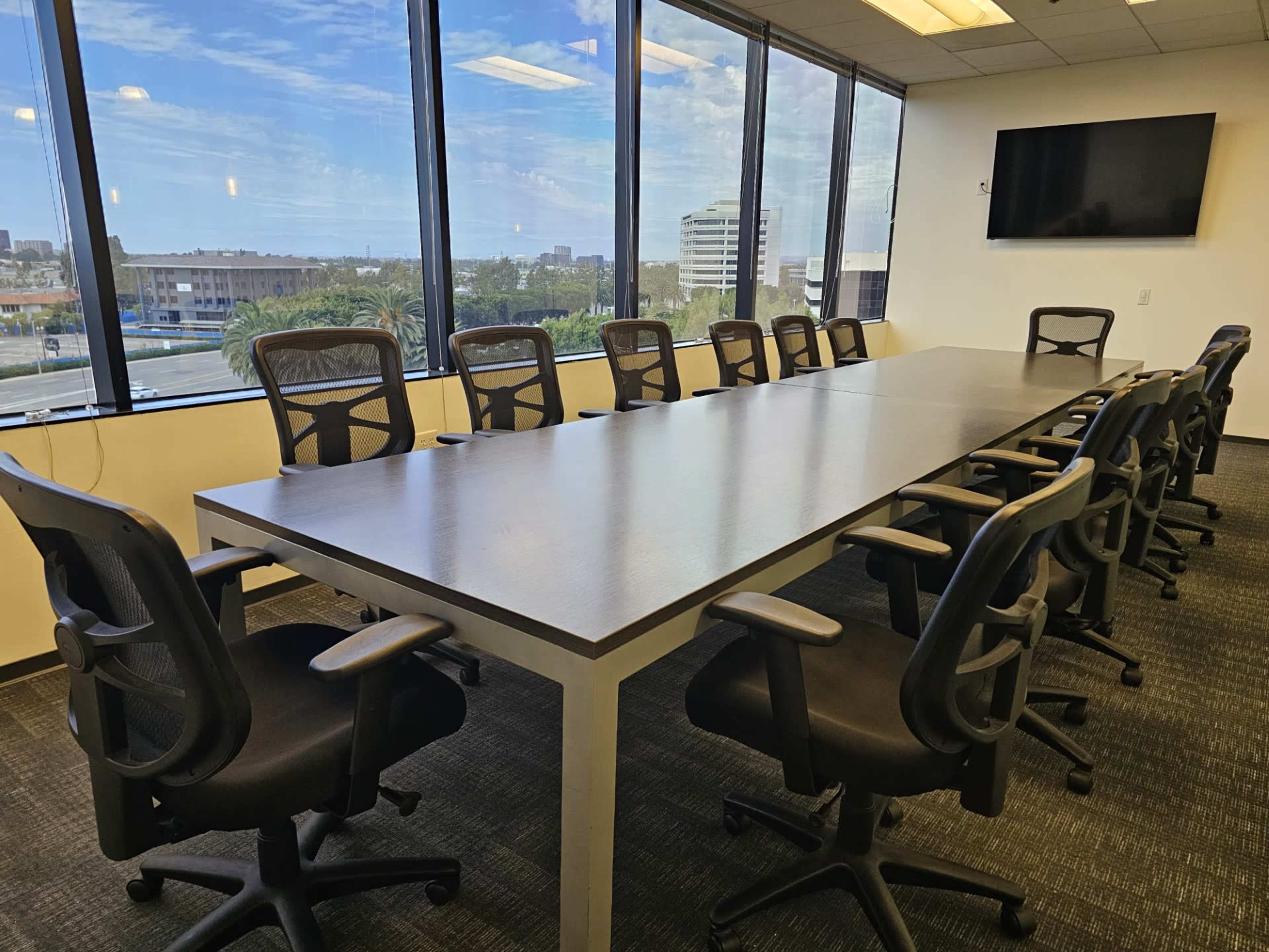 A large conference room features a long table surrounded by ergonomic office chairs, with windows overlooking a cityscape.