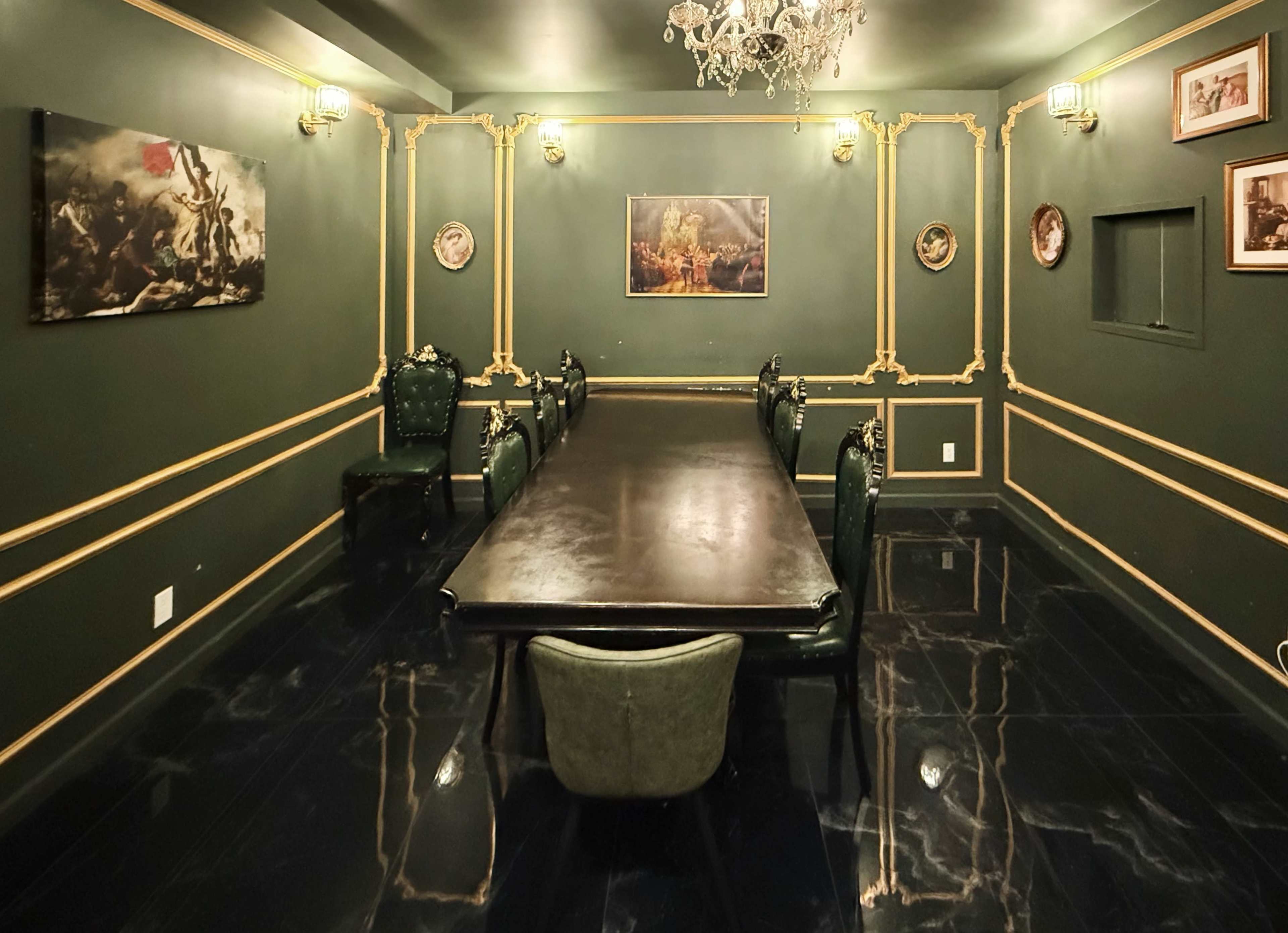 The image shows a dimly lit conference room with a long black table surrounded by dark green chairs and decorated with ornate wall moldings and framed artwork.