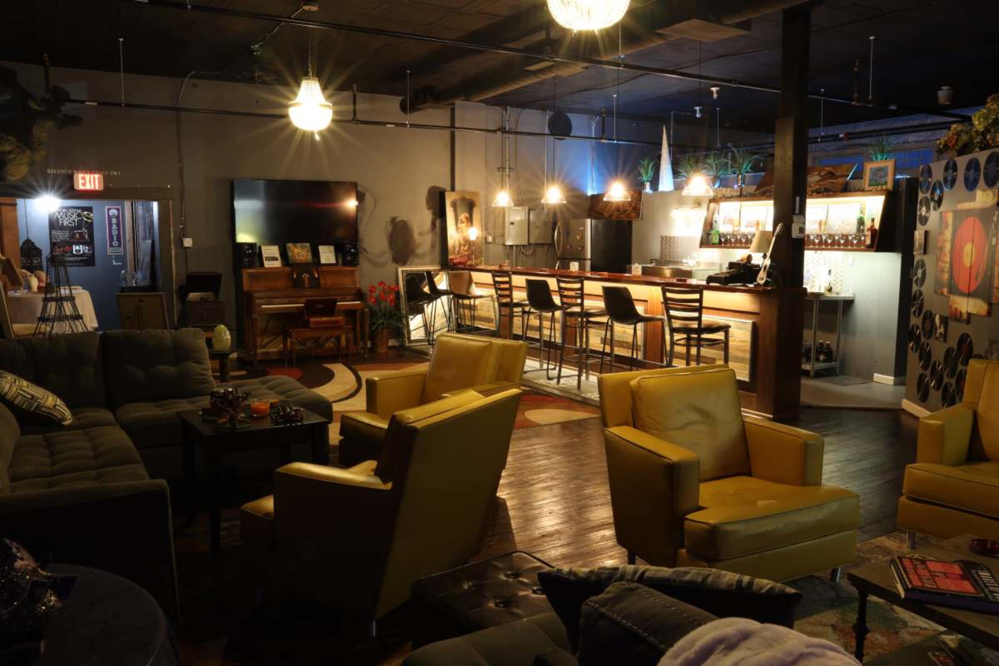 The image shows a modern lounge area with yellow armchairs, a bar, and a mix of comfortable seating arrangements under warm lighting.