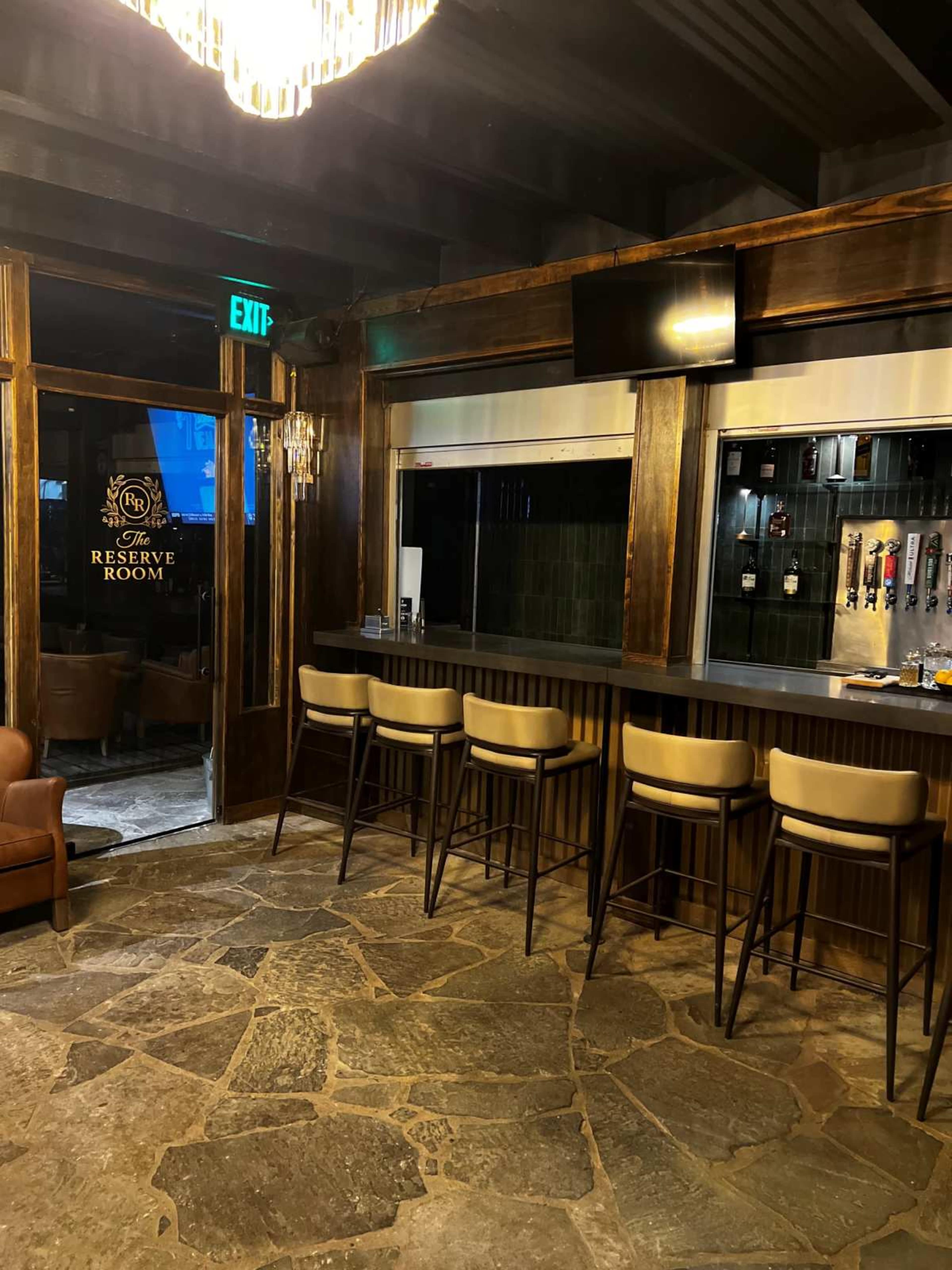 The image shows a bar area with high stools, a stone floor, and a glass entrance door labeled "Reserve Room."