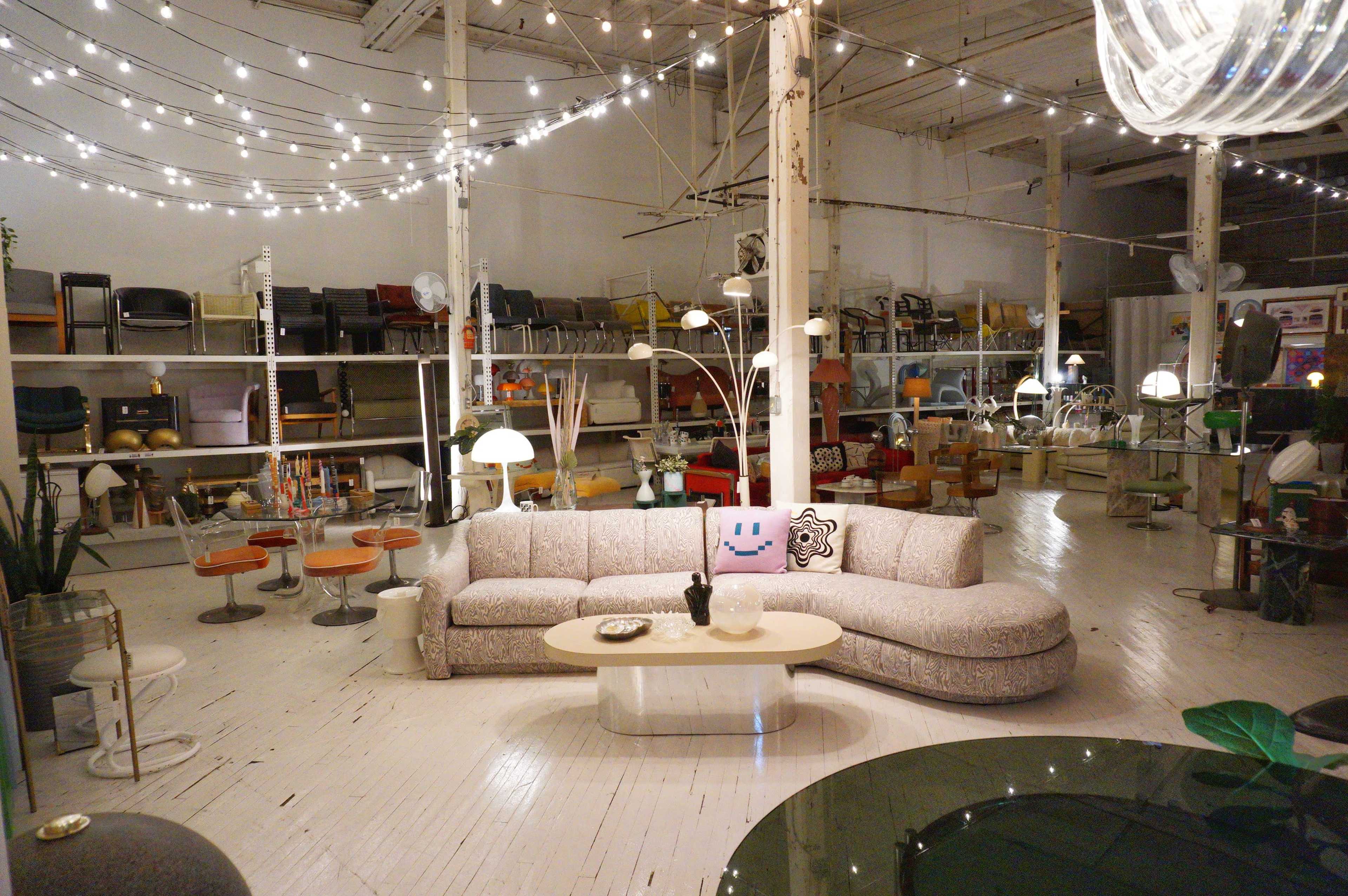 A spacious interior showcases a variety of modern furniture, including a large curved sofa, stylish lighting fixtures, and numerous seating options arranged around tables.