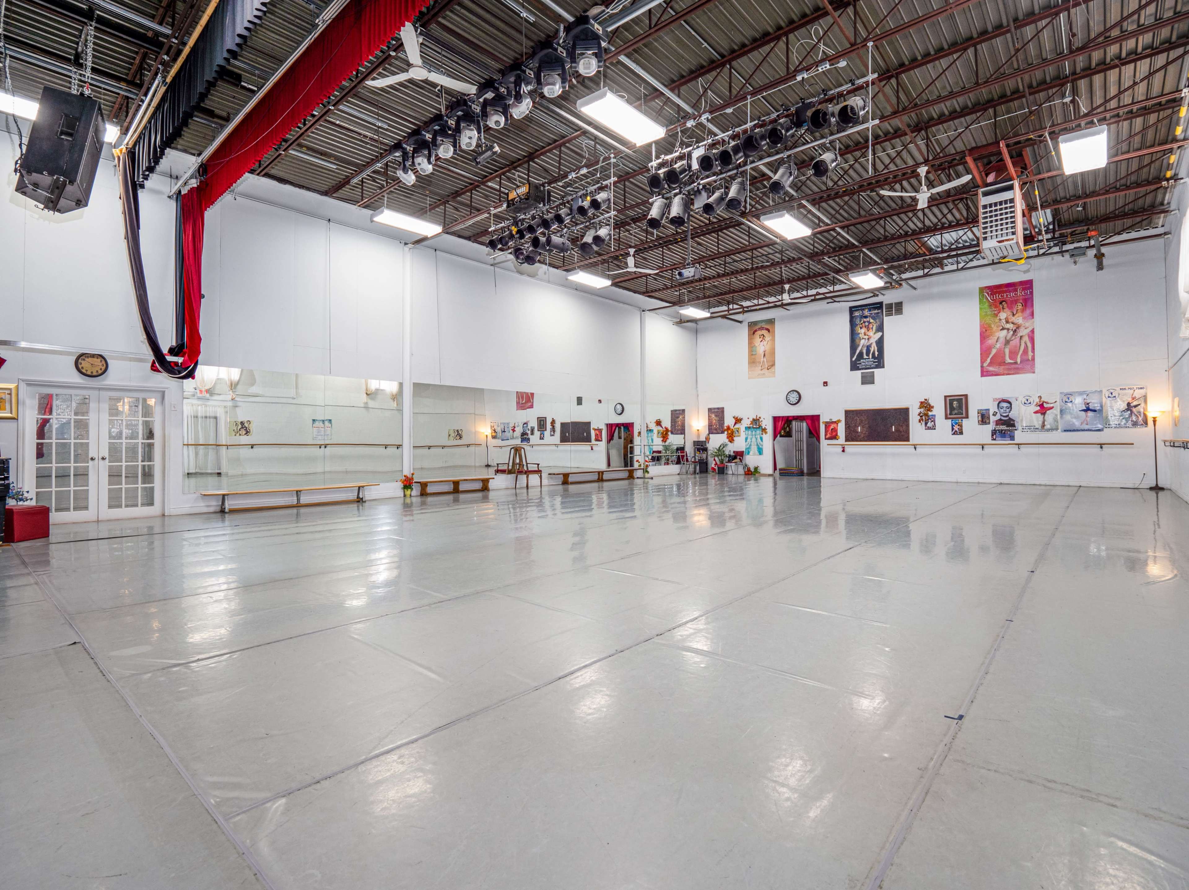 A spacious dance studio with a mirrored wall, wooden ballet bars, and various posters on the walls.