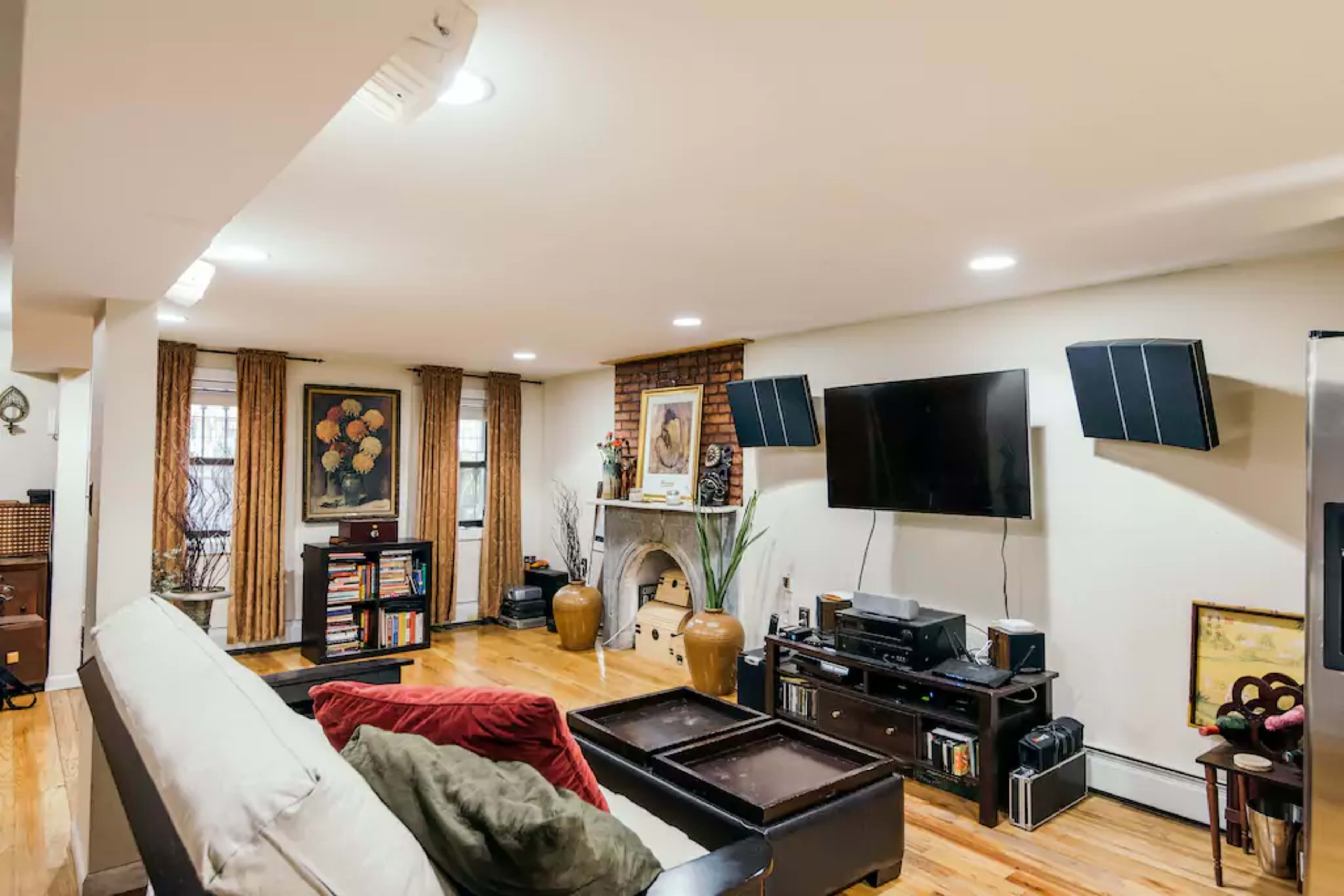 The image shows a living room with a television mounted on the wall, a fireplace, wooden flooring, and furniture arranged around a coffee table.