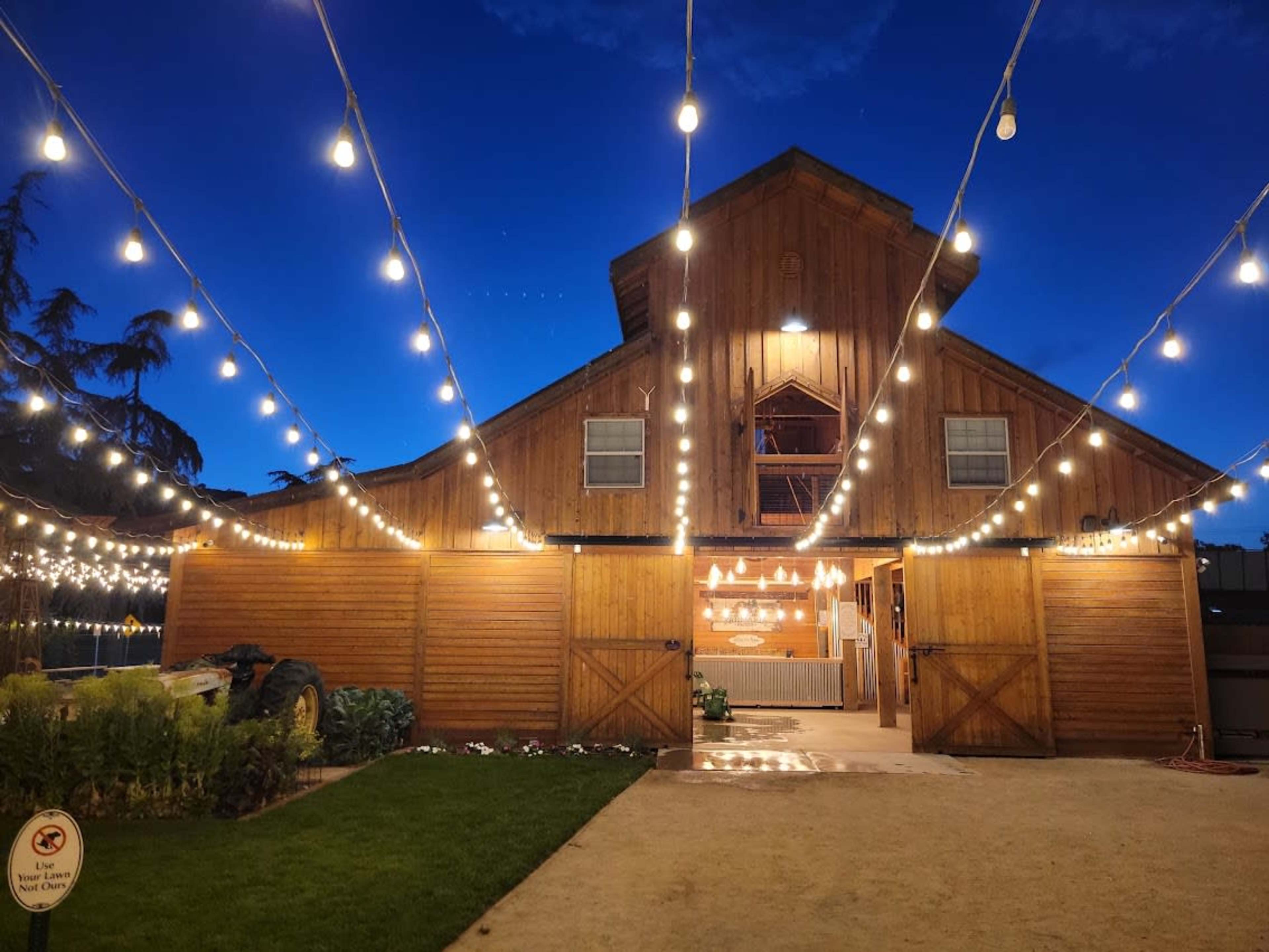 A wooden barn with string lights is illuminated under a blue evening sky.
