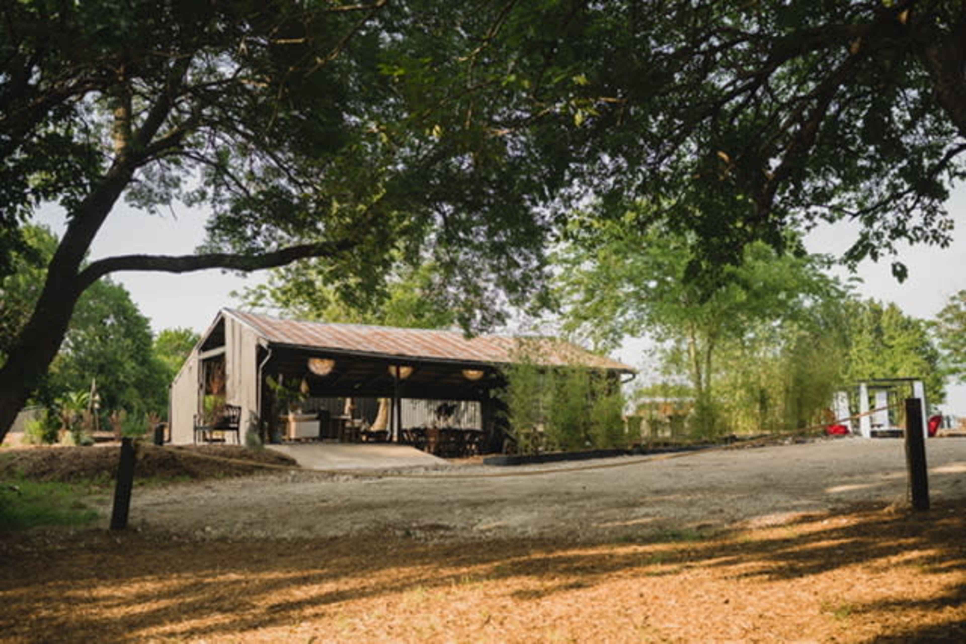 A rustic building with a metal roof is set among lush trees and gravel pathways.