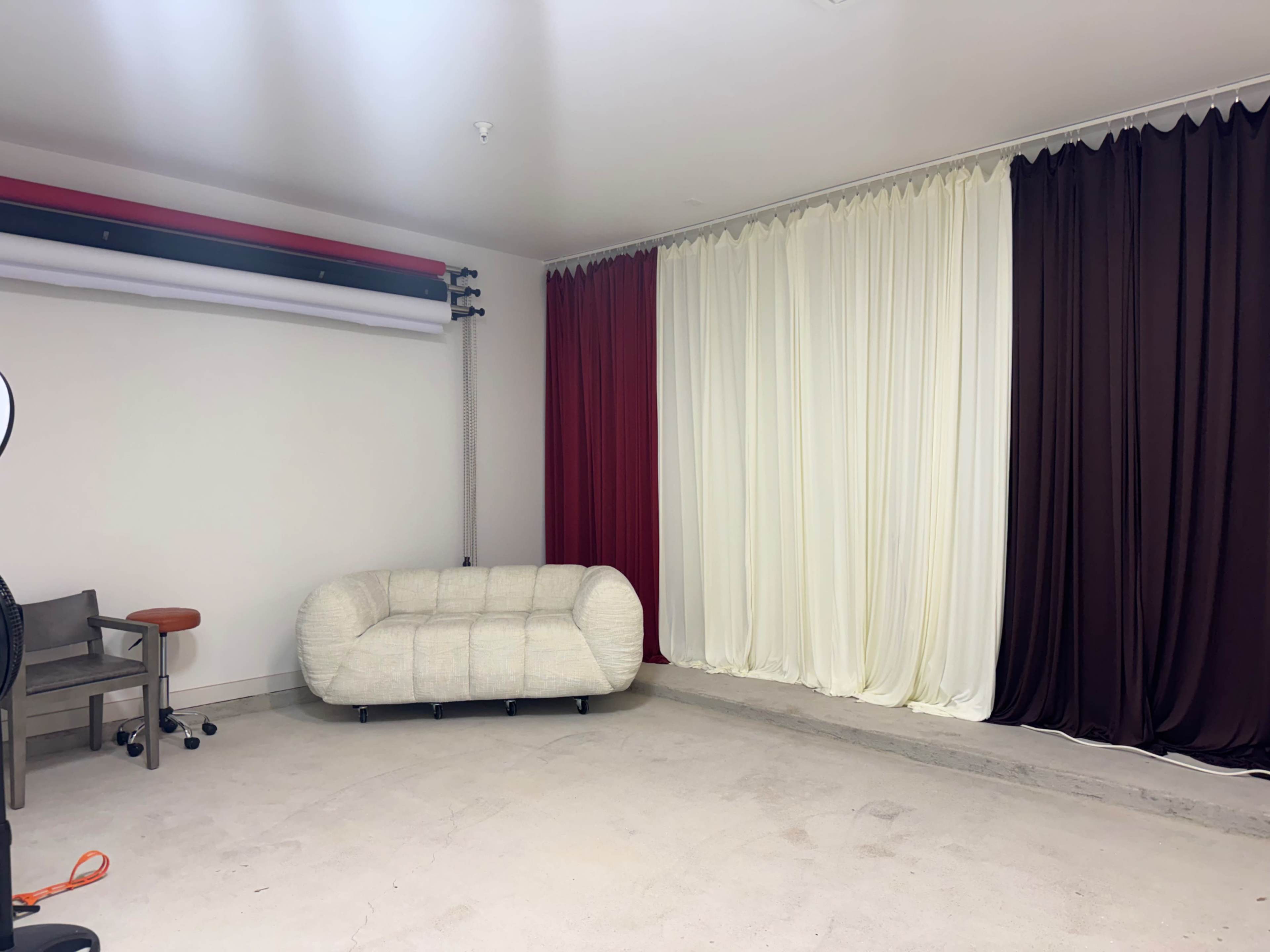 The image shows a spacious room with a white couch and draped curtains in red, white, and brown against one wall.