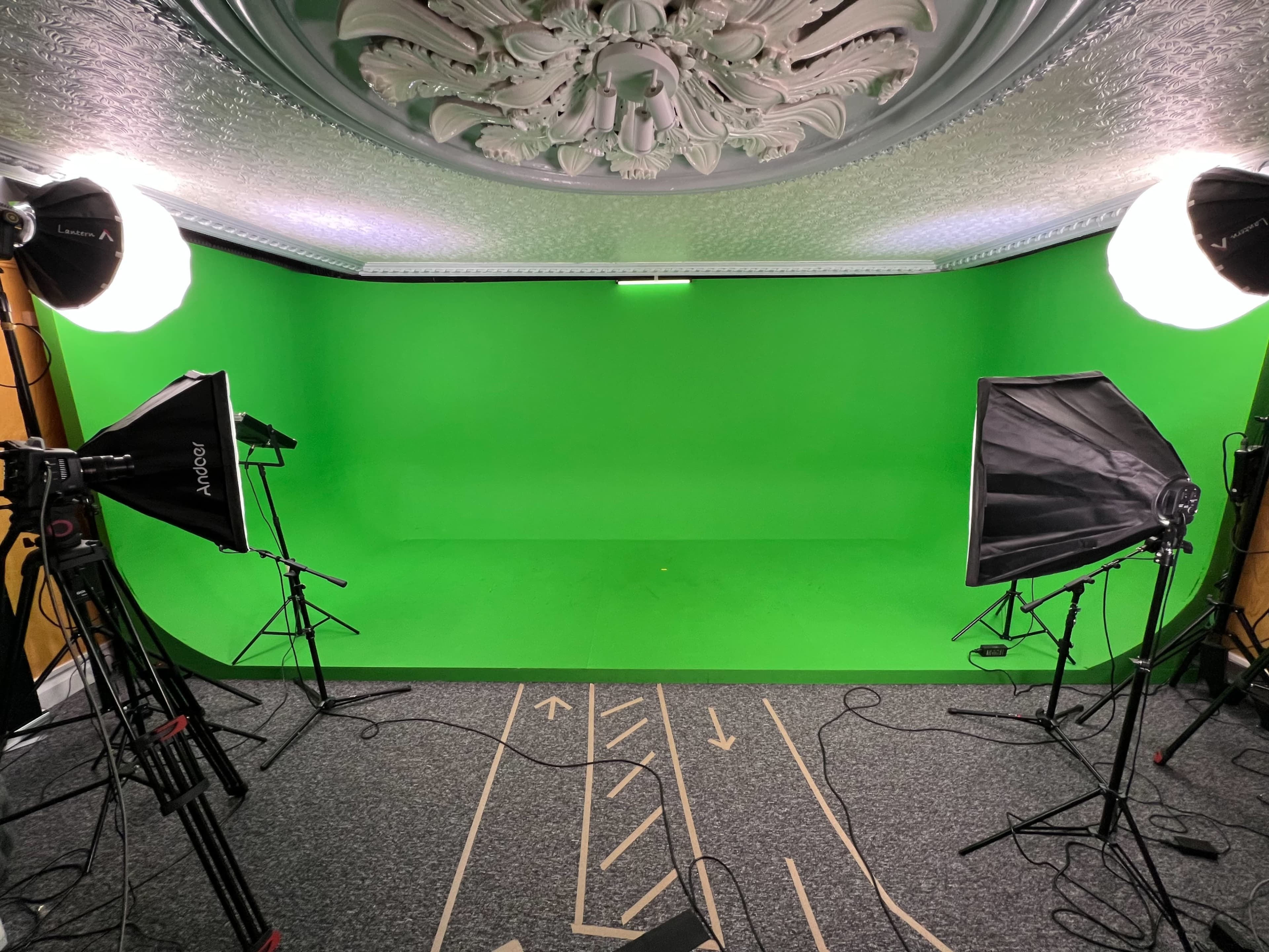The image shows a green screen studio setup with two lighting fixtures and a patterned floor in front of a green backdrop.