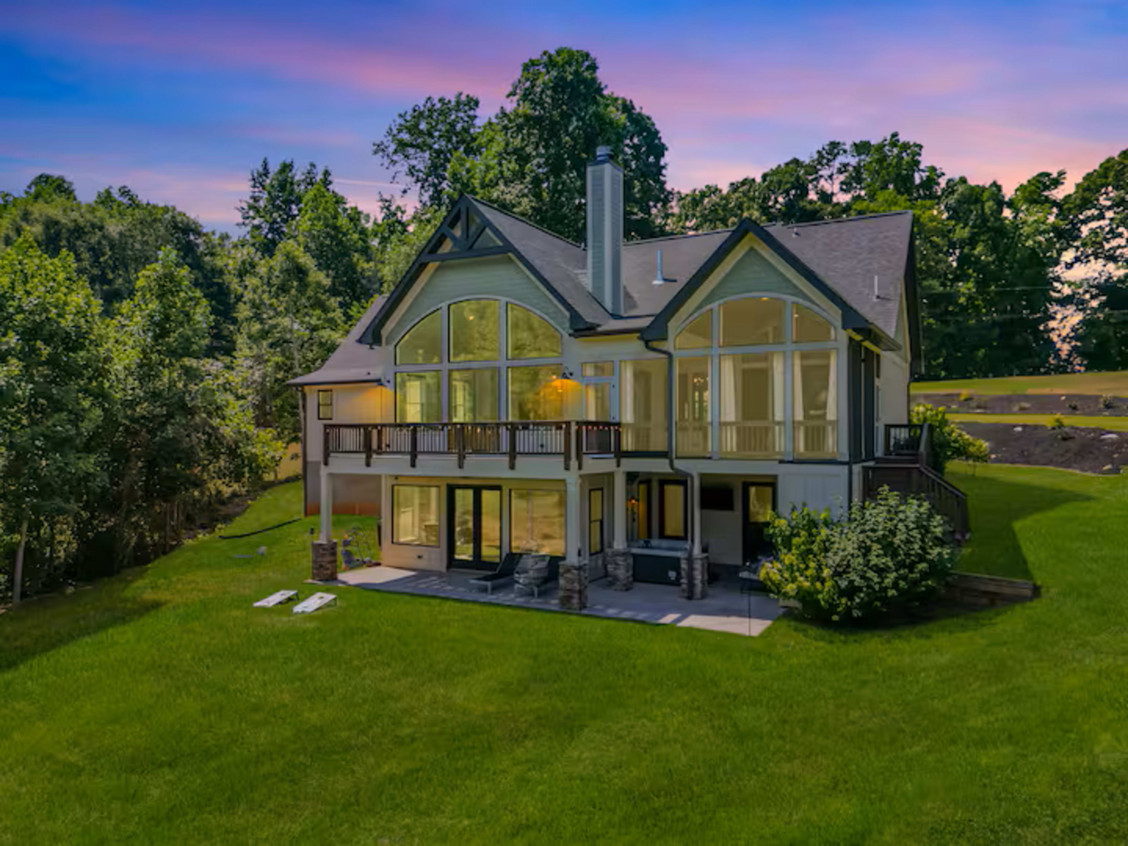 The image shows a large, modern house with expansive windows and a spacious backyard surrounded by trees.