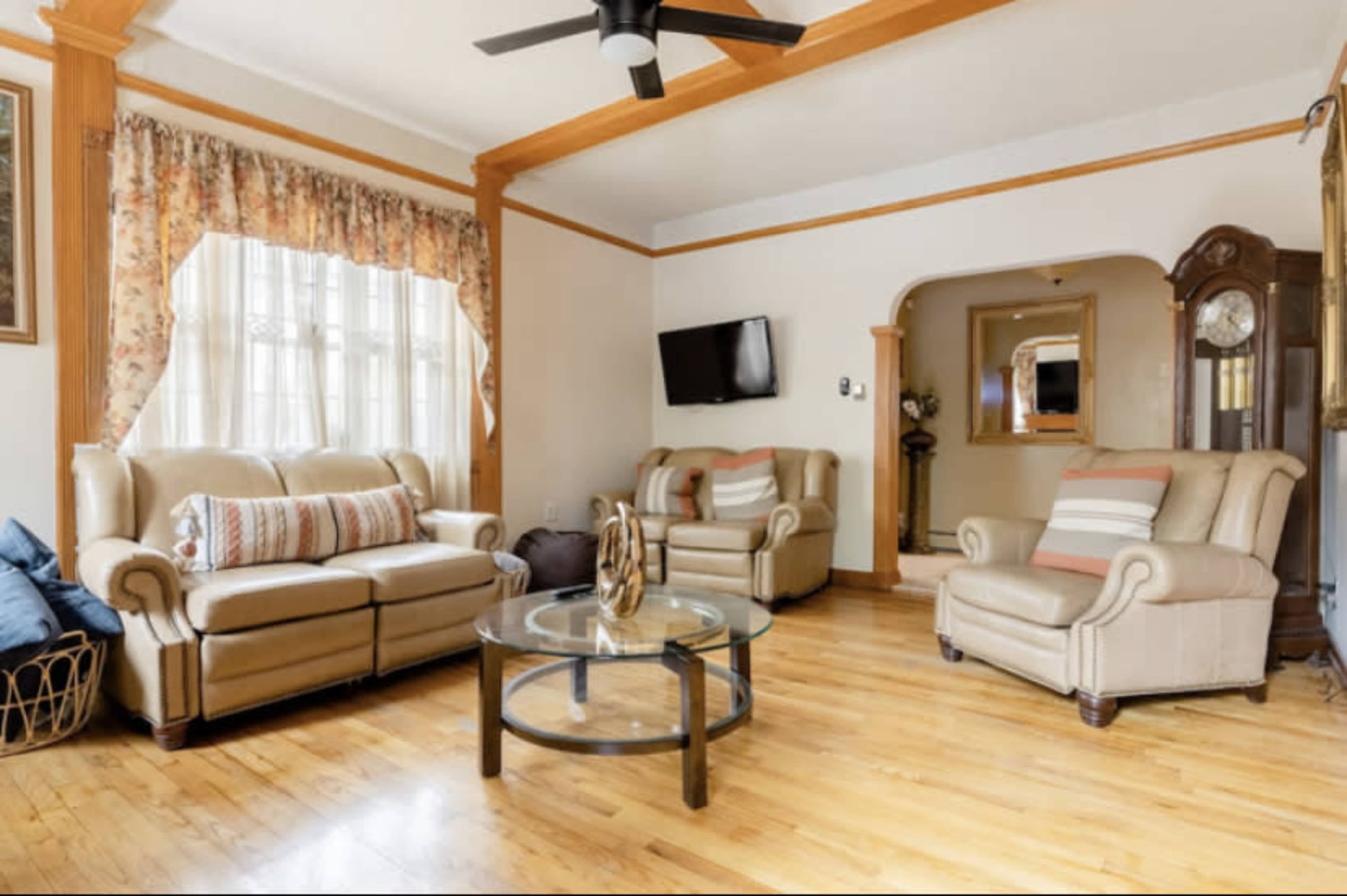 A living room with two beige sofas, a glass coffee table, and a television mounted on the wall, all set on a wooden floor.