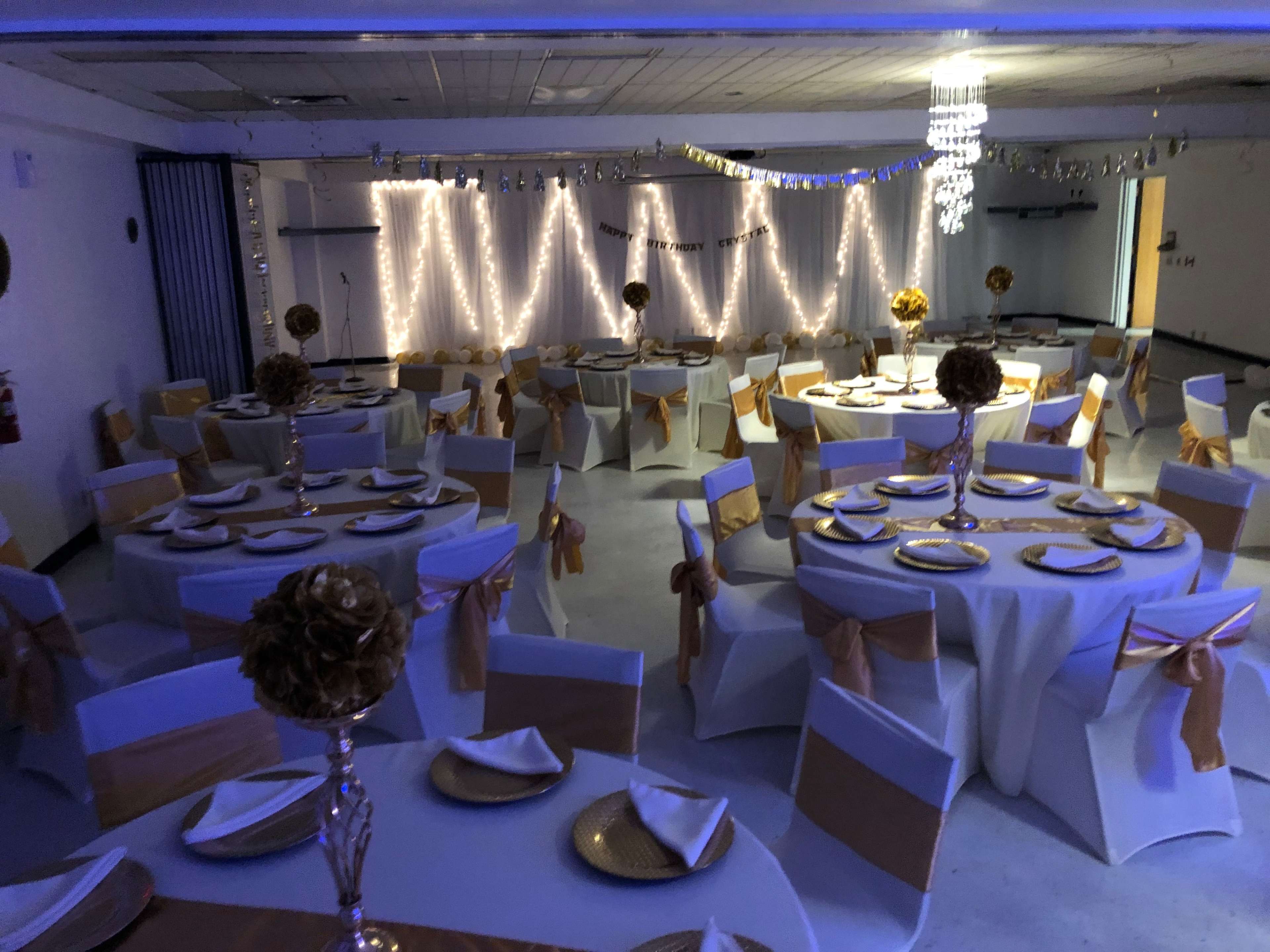 A banquet hall set up for an event, featuring round tables adorned with white tablecloths and gold accents, and decorated with floral centerpieces.