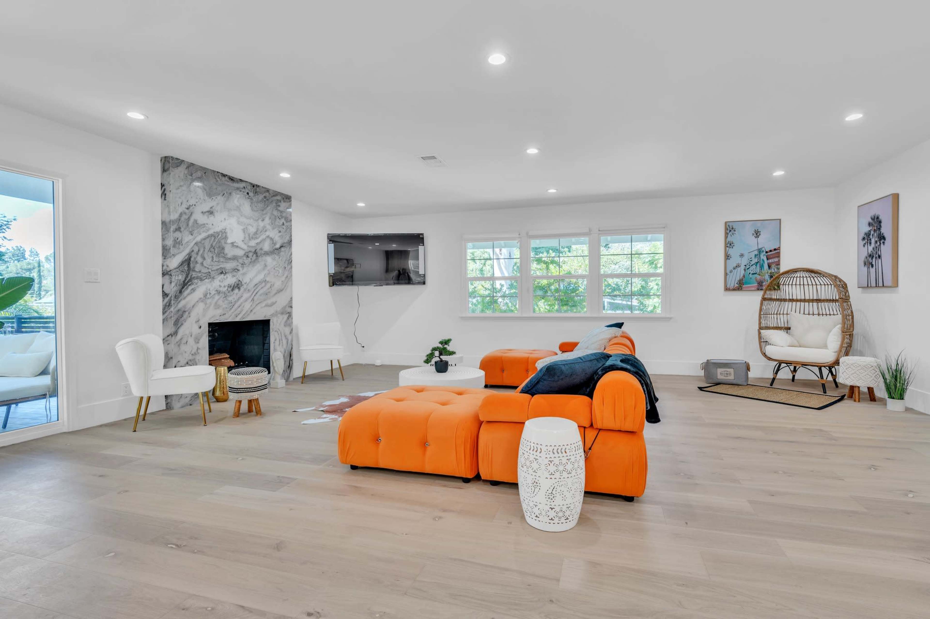 A spacious living room features an orange sectional sofa, a marble accent wall, and large windows allowing natural light.
