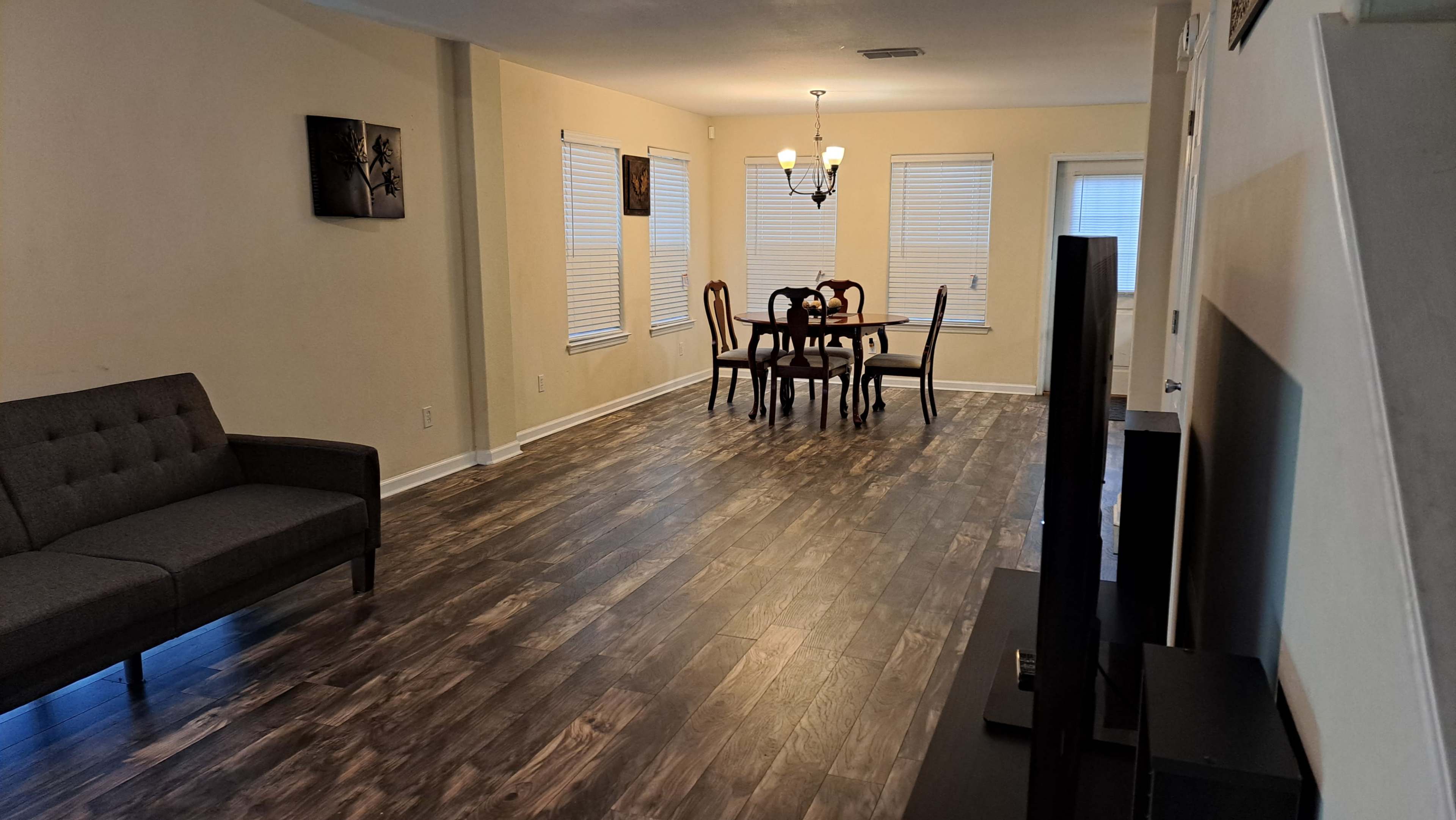 A spacious living area with a gray couch, dining table, and several windows allowing natural light.