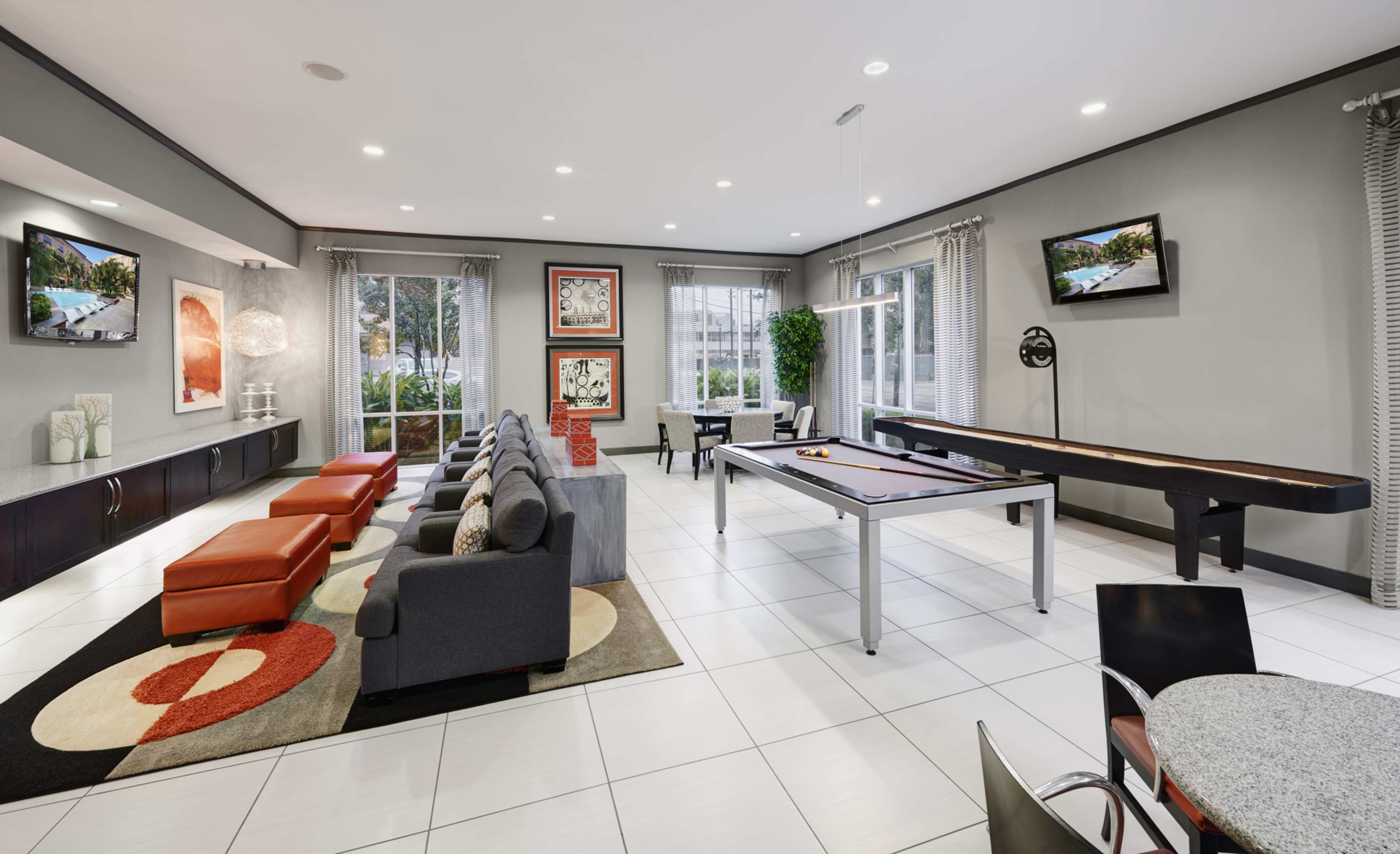 A modern lounge area with a pool table, seating, and large windows overlooking an outdoor view.