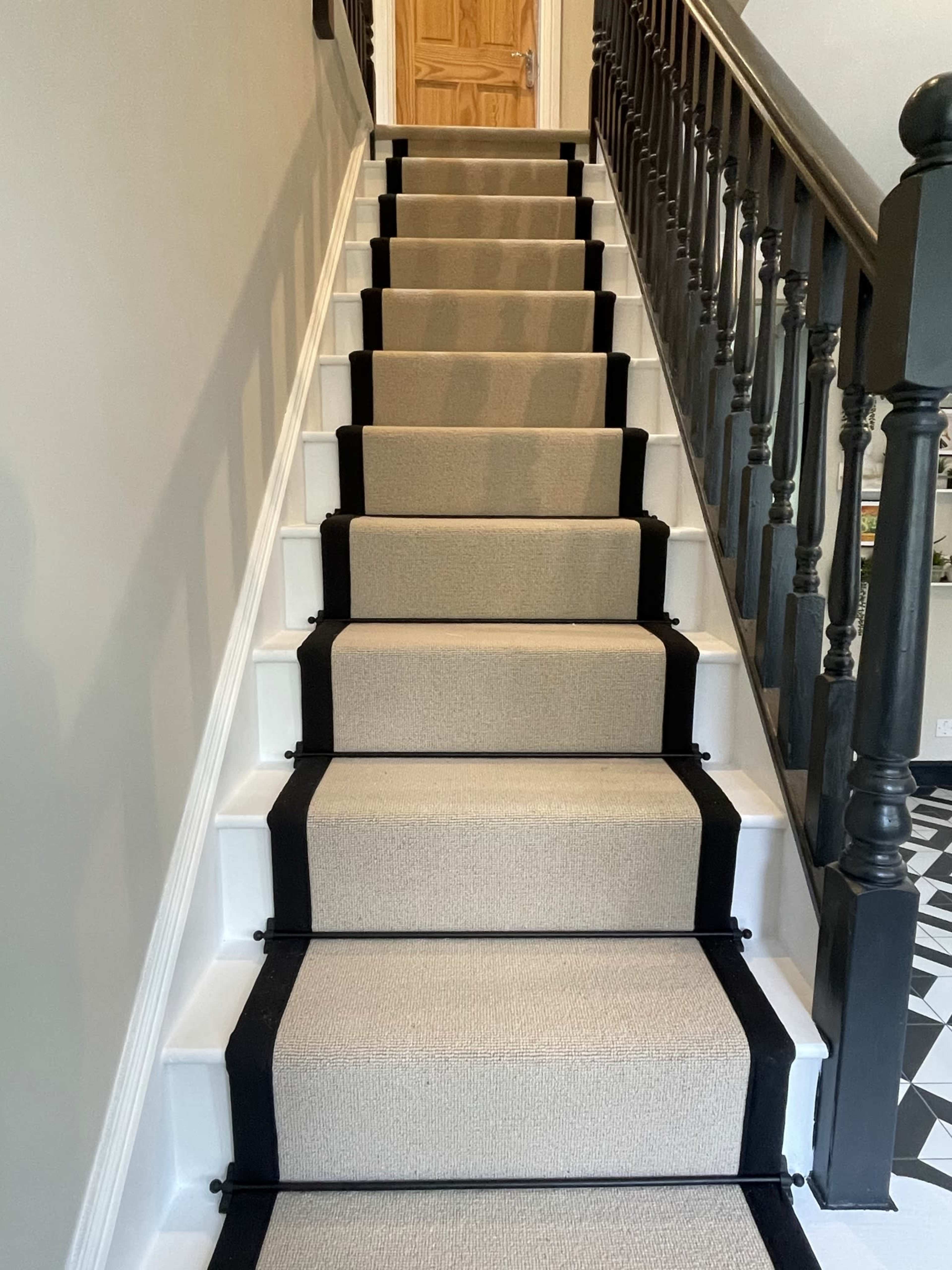 A staircase with beige carpet runners bordered by black stripes, leading up to a wooden door.