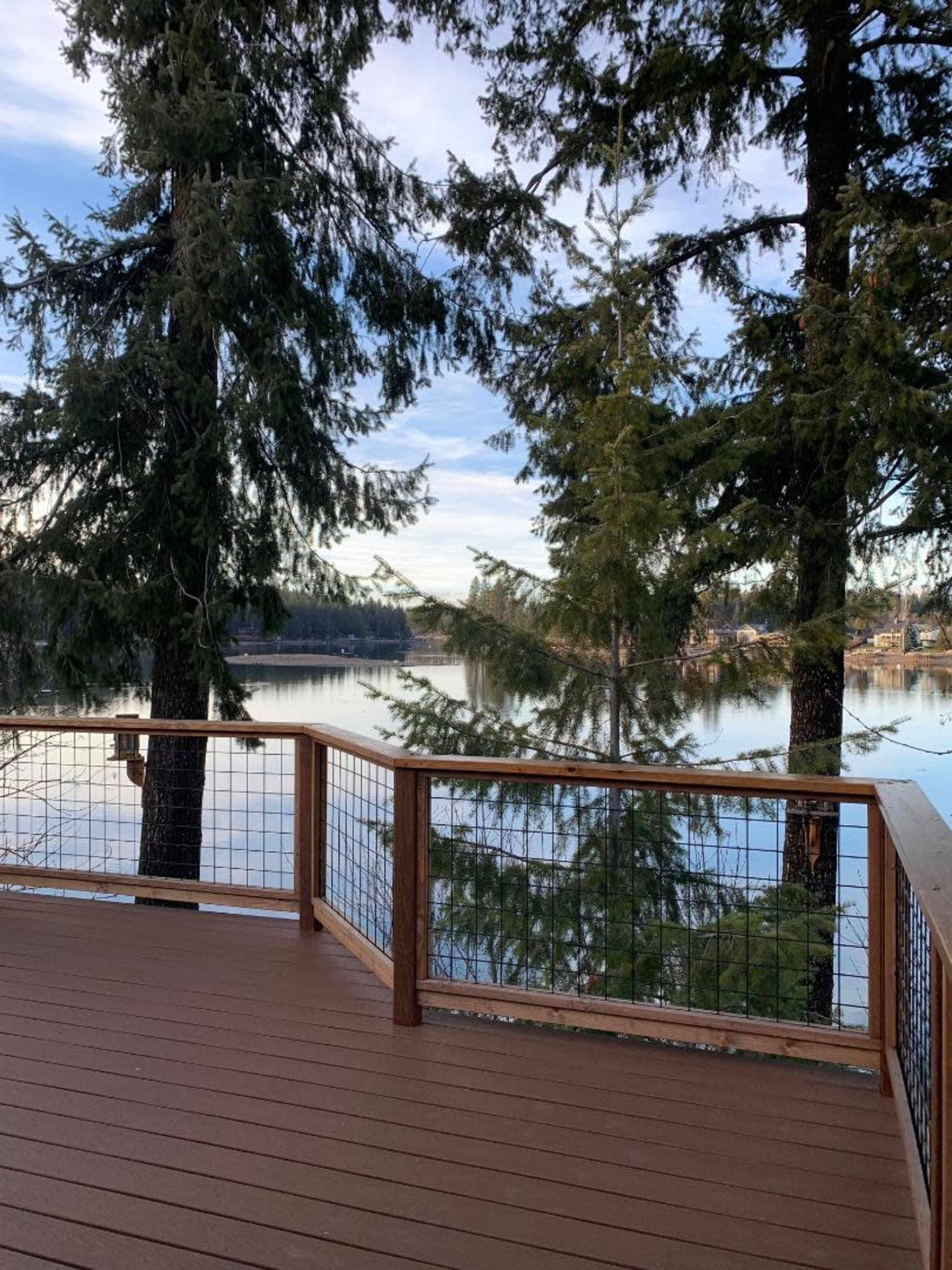 A wooden deck overlooks a calm lake surrounded by tall evergreen trees.
